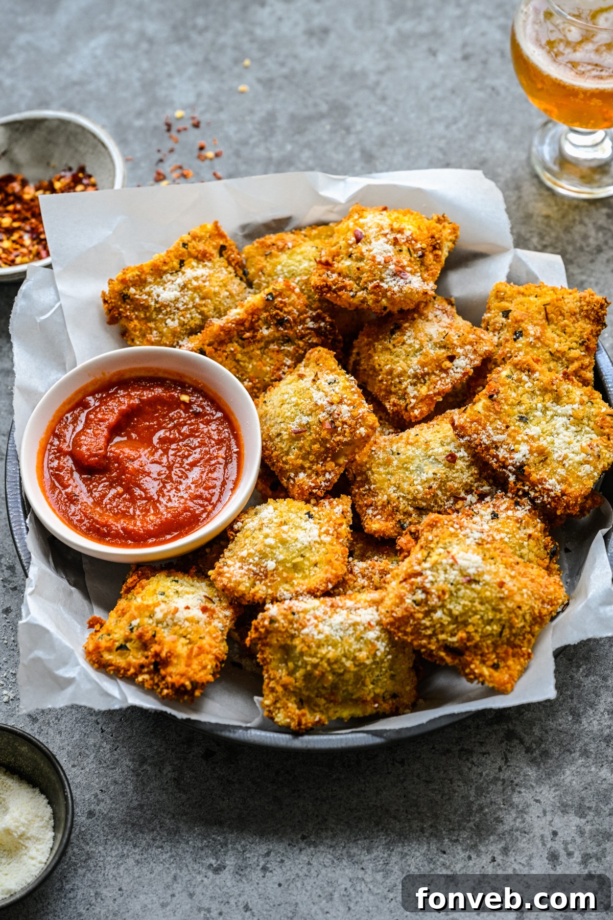 Side view of Air Fryer Ravioli in a black serving tray with parchment paper and marinara sauce. 
