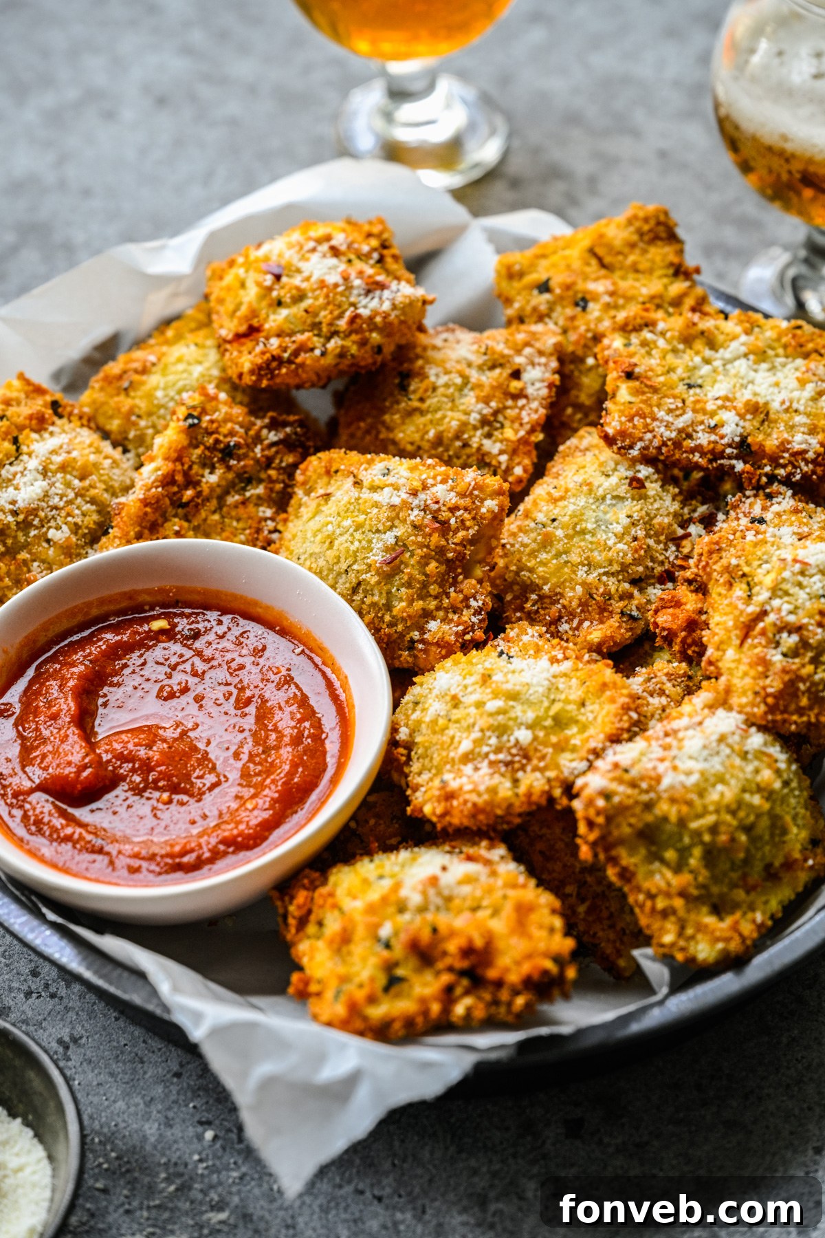 Side view of Air Fryer Ravioli in a black serving tray with parchment paper and marinara sauce. 