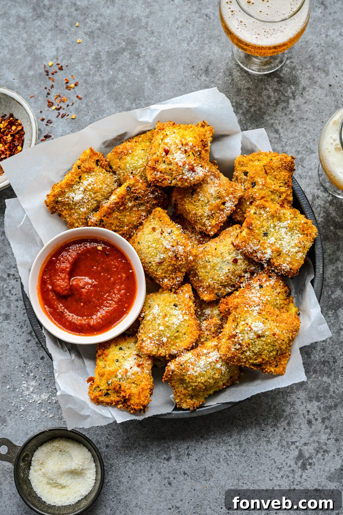 Overhead view of Air Fryer Ravioli in a black serving tray with parchment paper and marinara sauce. 