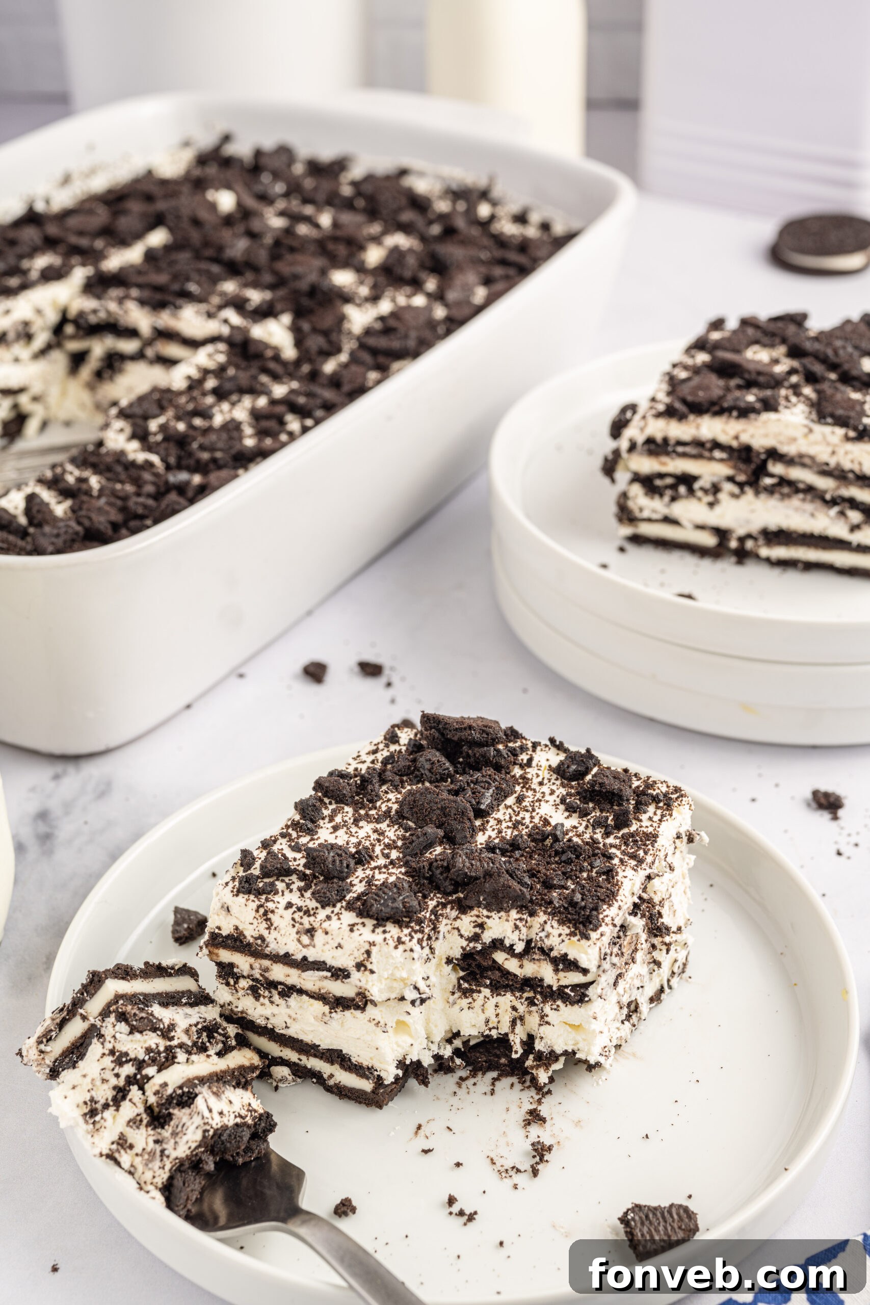 Front view of a slice of Oreo Icebox Cake on a white plate with a bite removed by a silver fork.