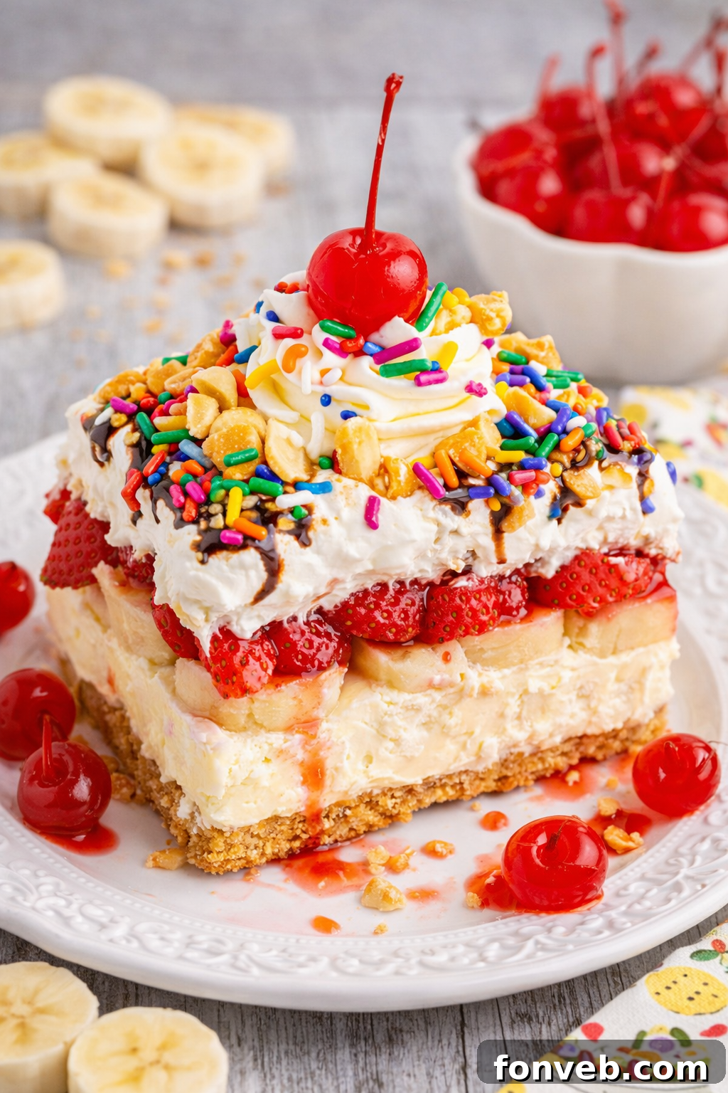 A perfectly sliced piece of No-Bake Banana Split Cake on a pristine white plate, showcasing its vibrant layers of crust, creamy filling, bananas, and a drizzle of chocolate.