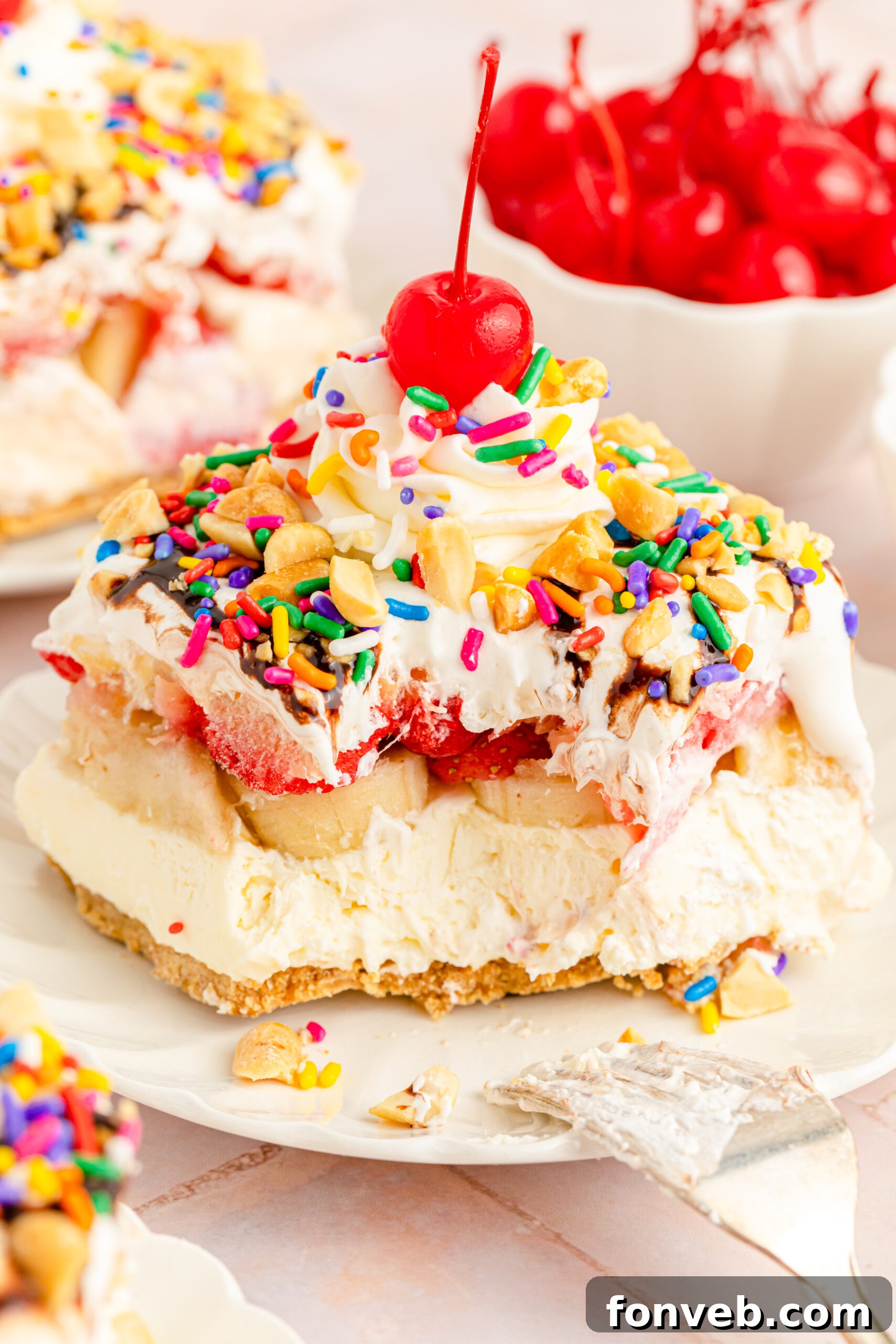A close-up of a delightful slice of No-Bake Banana Split Cake on a white plate, with a fork having taken a bite, showcasing the perfect combination of textures.