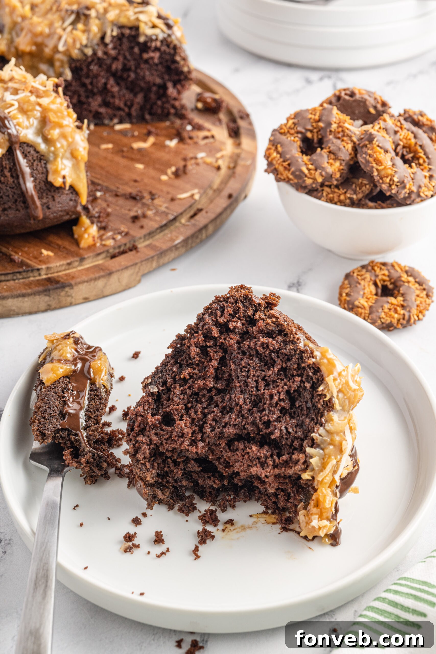 Front view of a slice of Samoa Cake on a white plate with a bite removed by a silver fork.