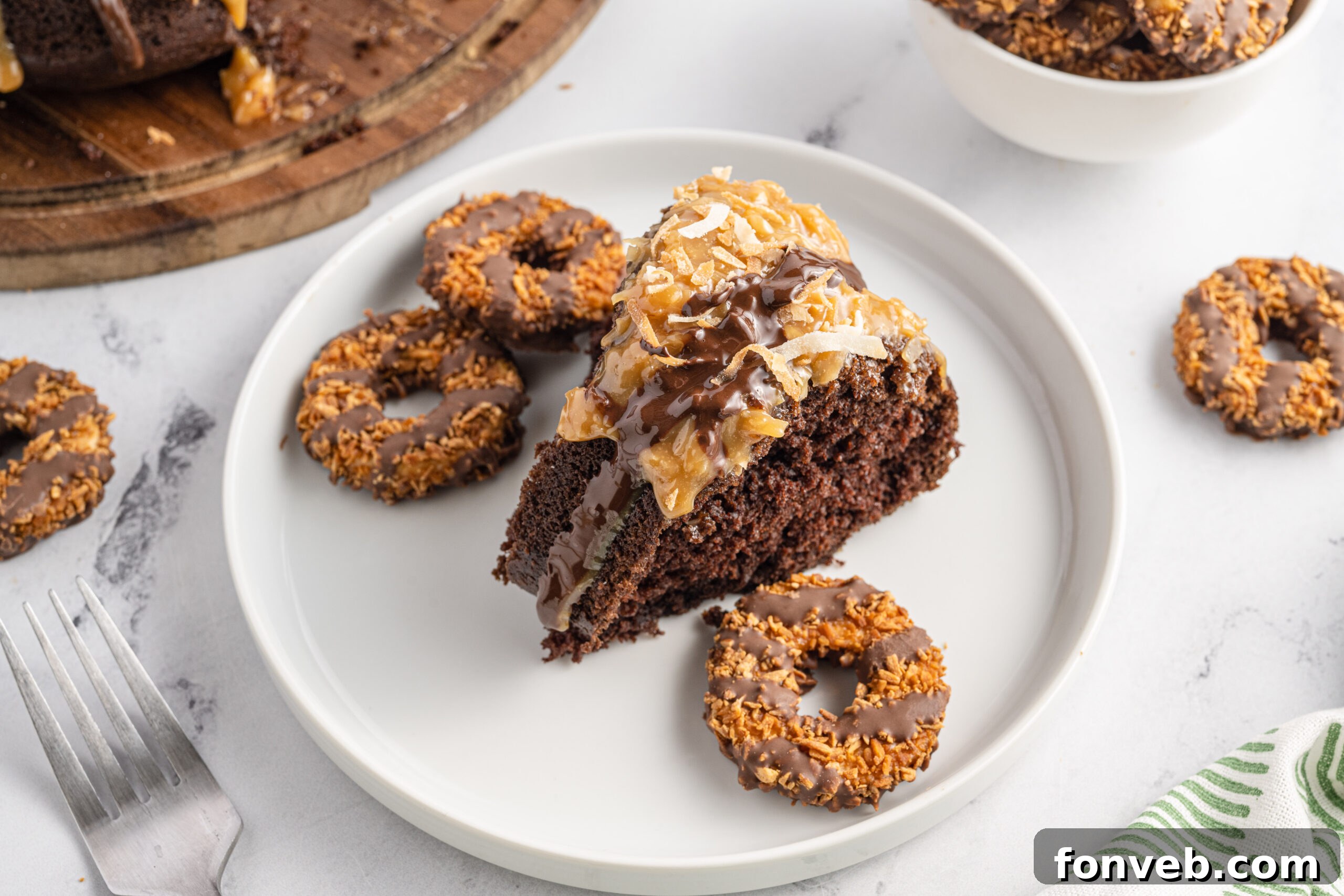 Close up view of a slice of Samoa Cake on a white plate with samoa cookies next to it