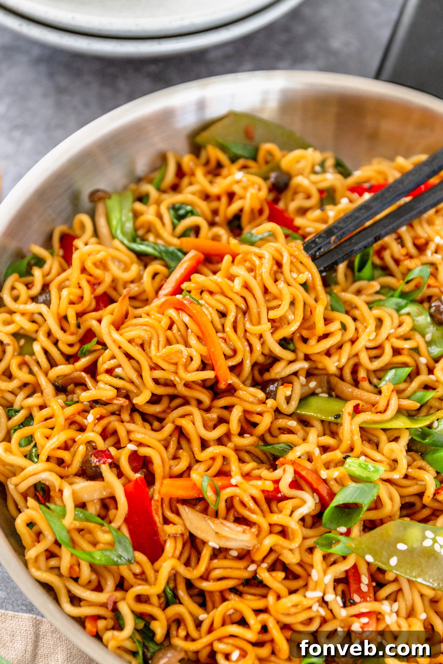 A pair of chop sticks removing Ramen Stir Fry from a silver frying pan. 