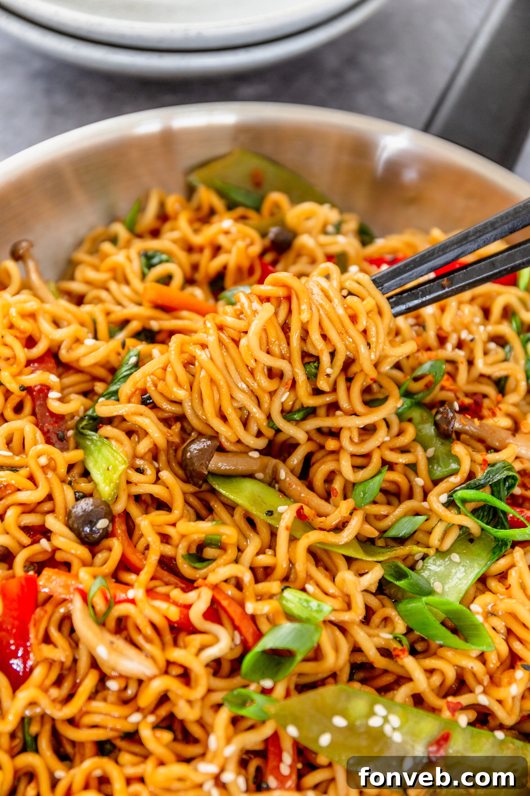 A pair of chop sticks lifting up a bite of the Ramen Stir Fry from a silver frying pan. 