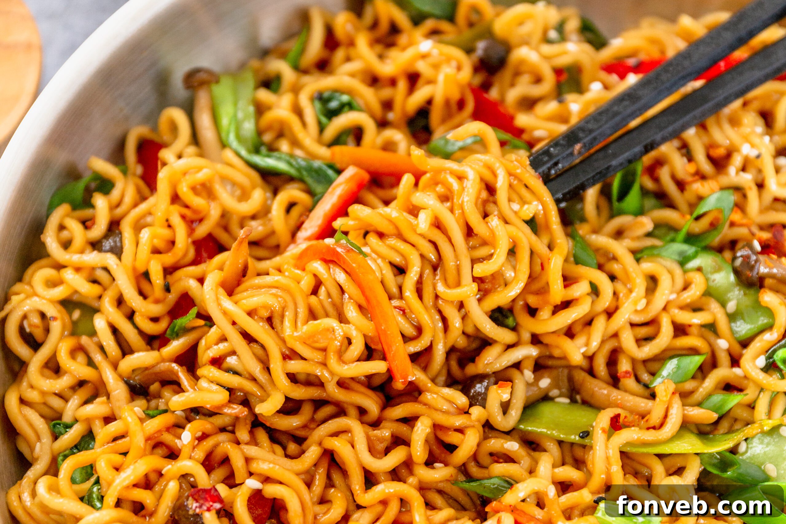 A pair of chop sticks removing Ramen Stir Fry from a silver frying pan. 