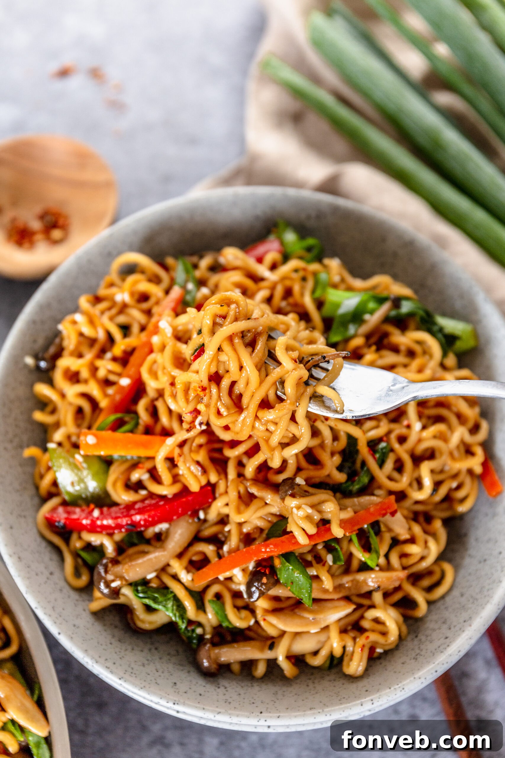 A fork removing Ramen Stir Fry from a speckled white bowl. 