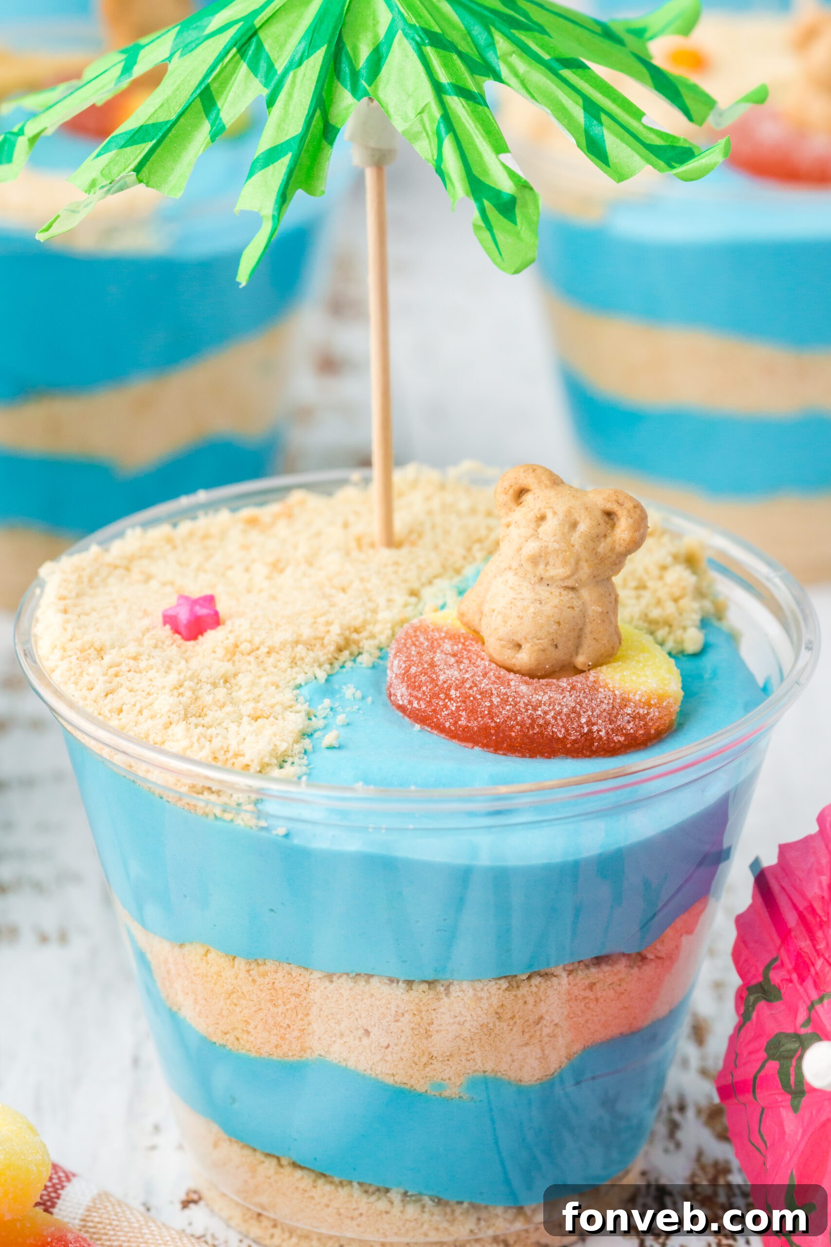 Close up view of the vibrant blue and tan layers in Beach Cheesecake Pudding Cups, topped with a gummy ring and teddy graham.