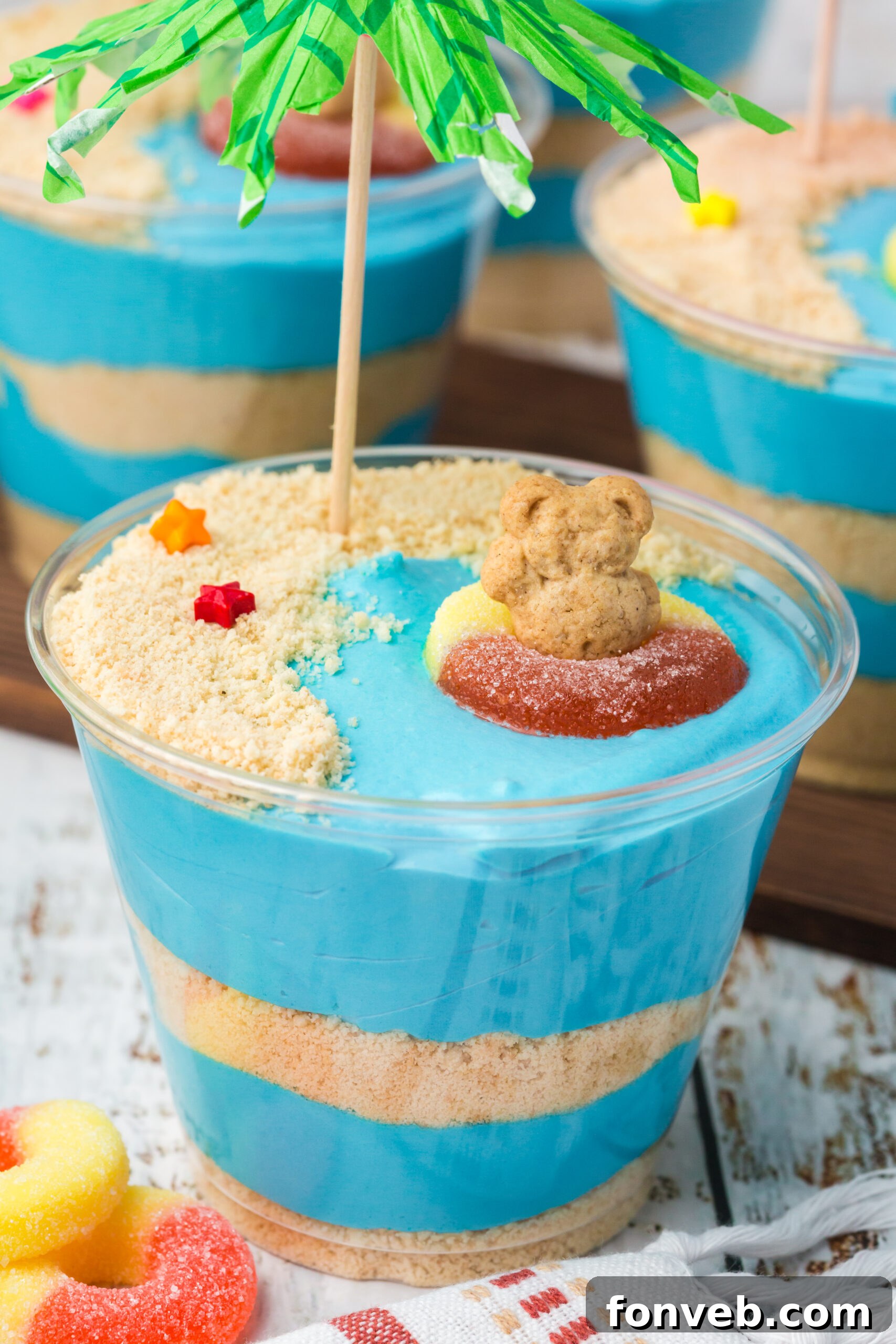Close up view of Beach Cheesecake Pudding Cups with a green umbrella, placed on a white table.