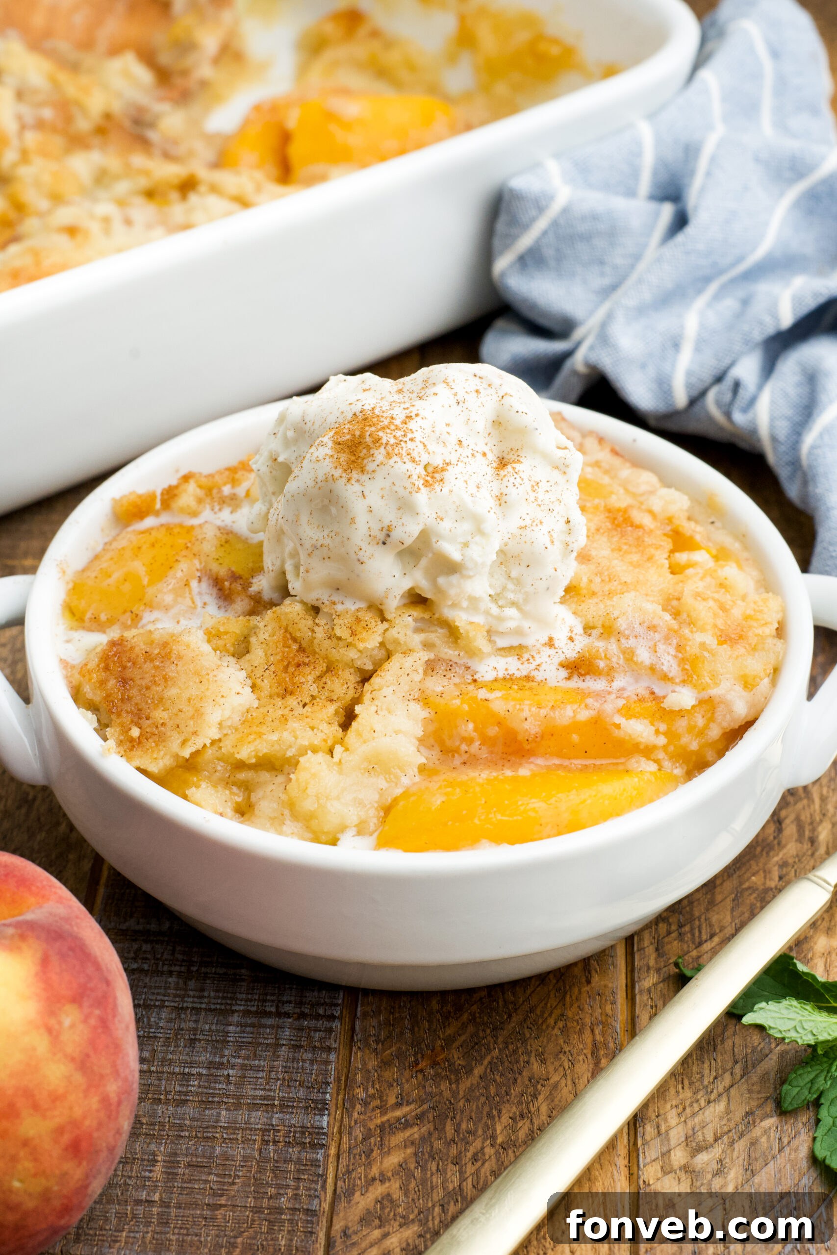 Simple Peach Dump Cake 2 Front view of a serving of Peach Dump Cake in a white bowl topped with a scoop of vanilla ice cream.