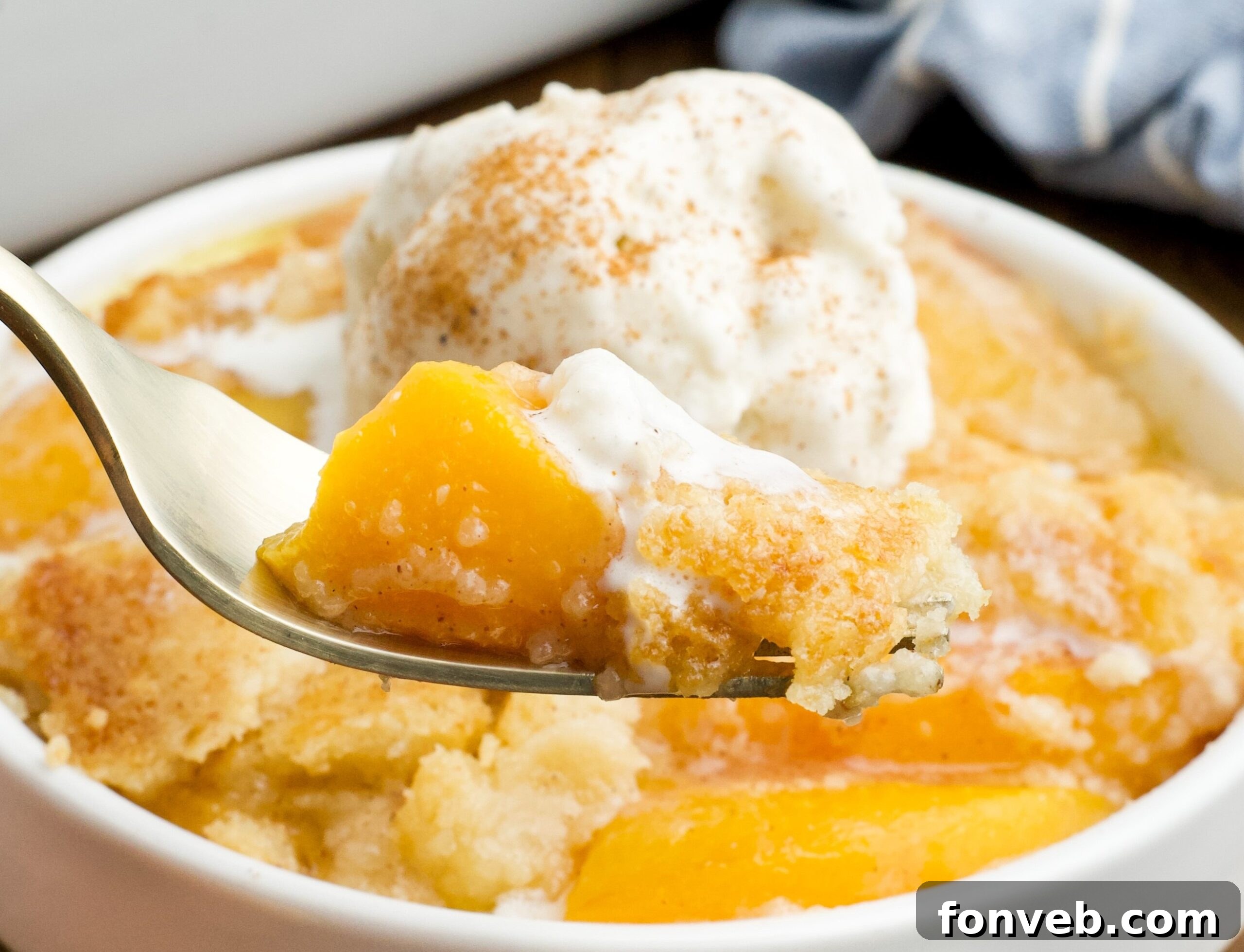 Simple Peach Dump Cake 14 close up of of a serving of Peach Dump Cake in a white bowl with a gold fork removing a bite.