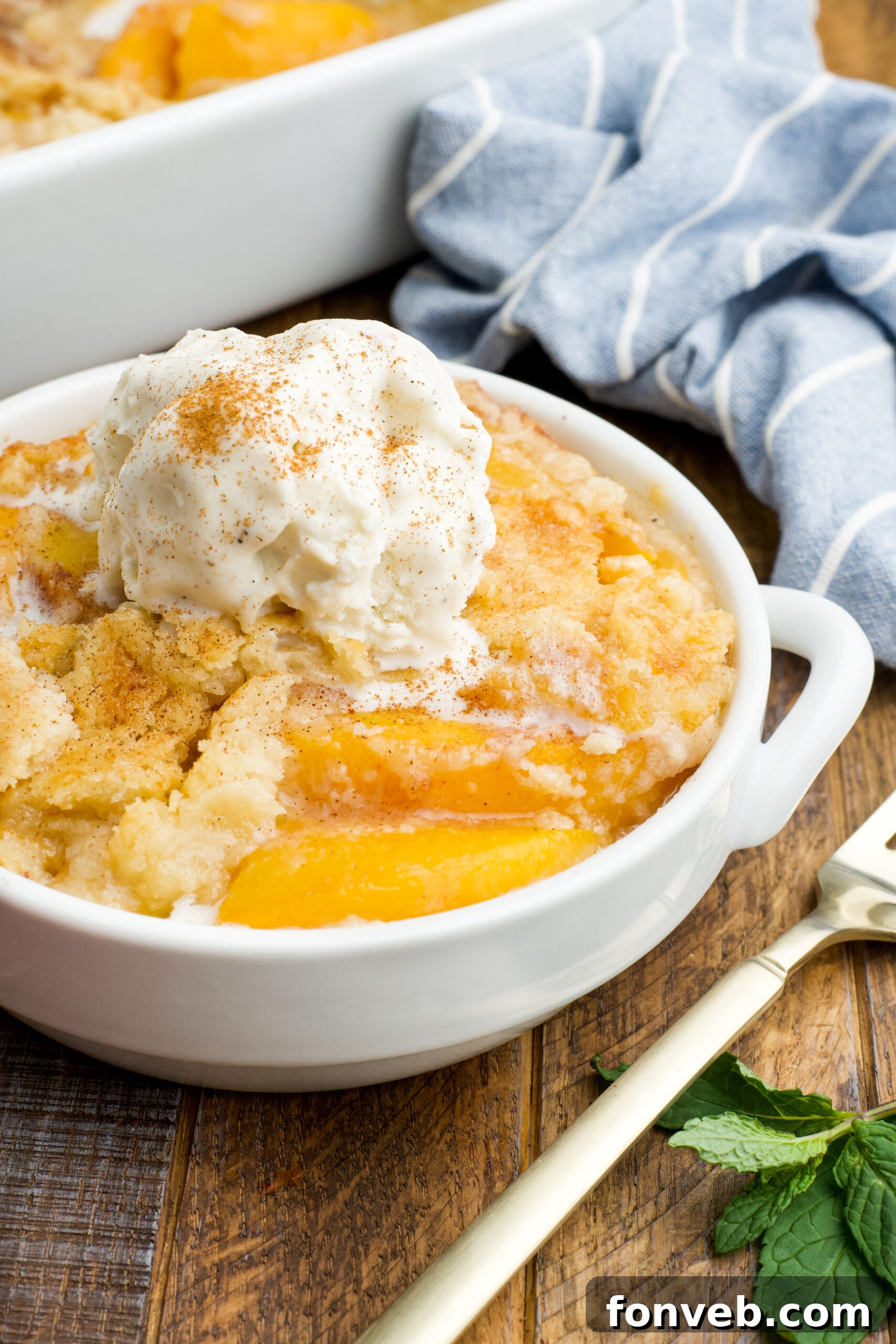 Simple Peach Dump Cake 16 Front view of a serving of Peach Dump Cake in a white bowl topped with a scoop of vanilla ice cream.