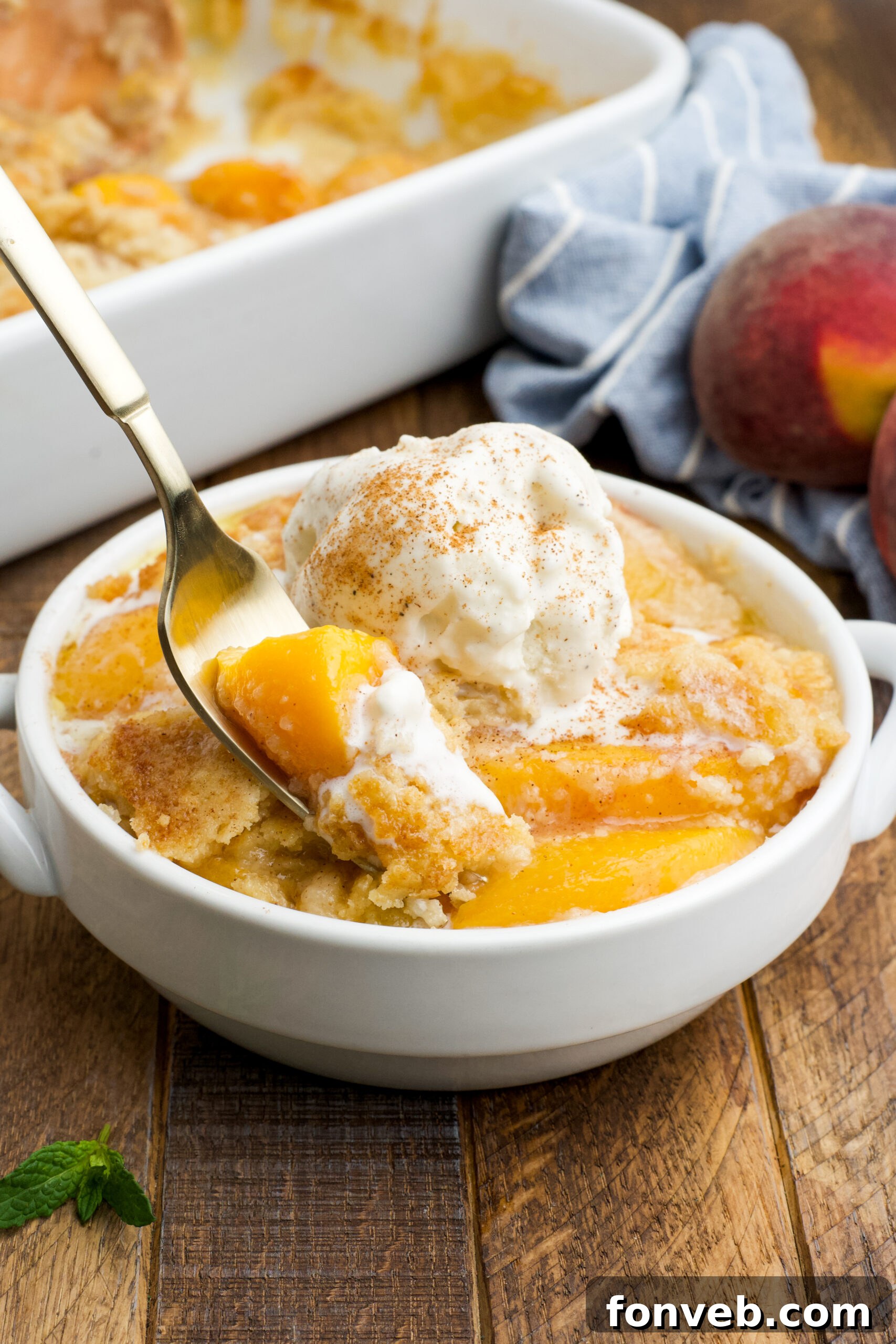 Simple Peach Dump Cake 18 Front view of a serving of Peach Dump Cake in a white bowl with a gold fork removing a bite.