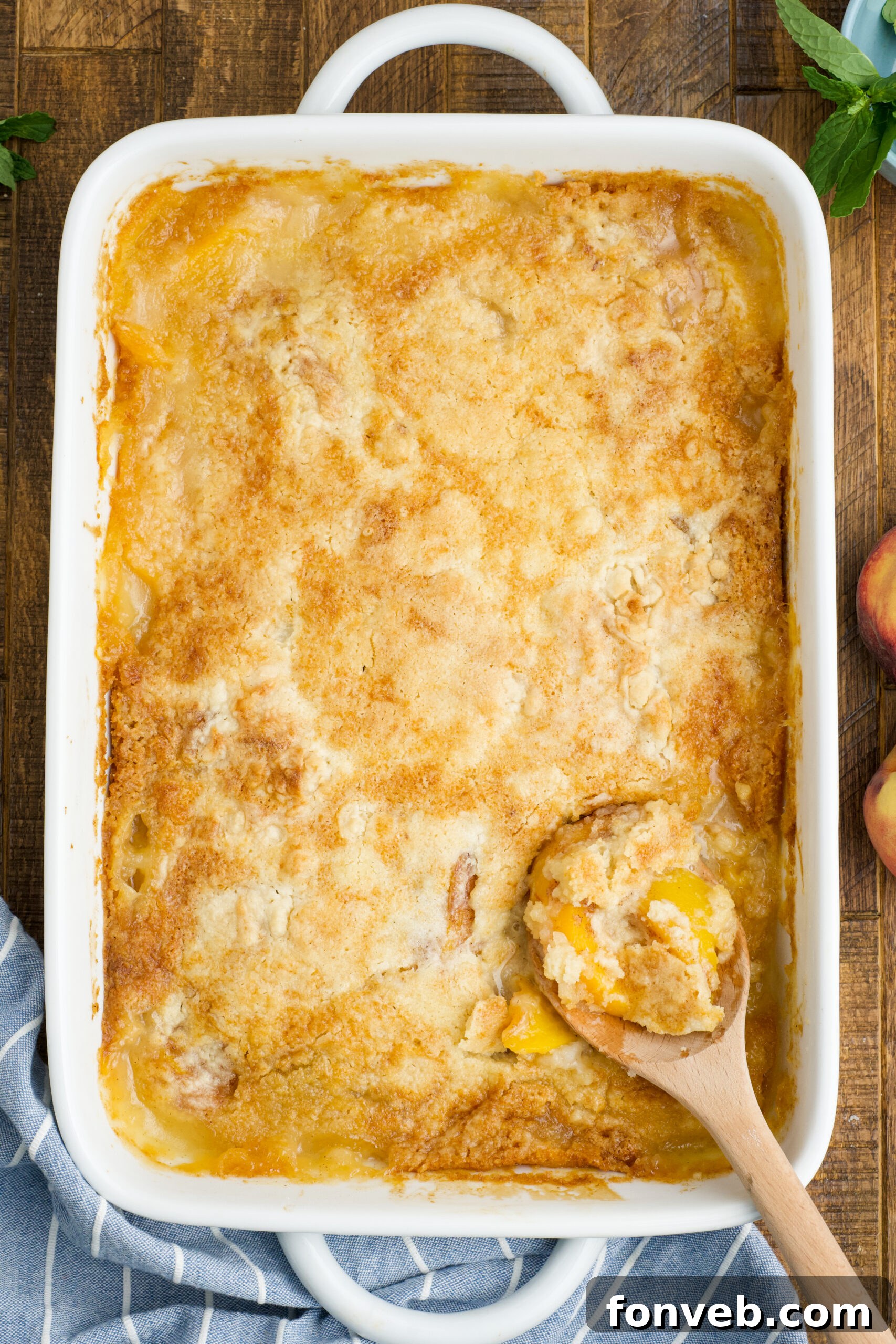 Simple Peach Dump Cake 4 Overhead view of Peach Dump Cake in a white baking dish with a wooden spoon removing a serving.