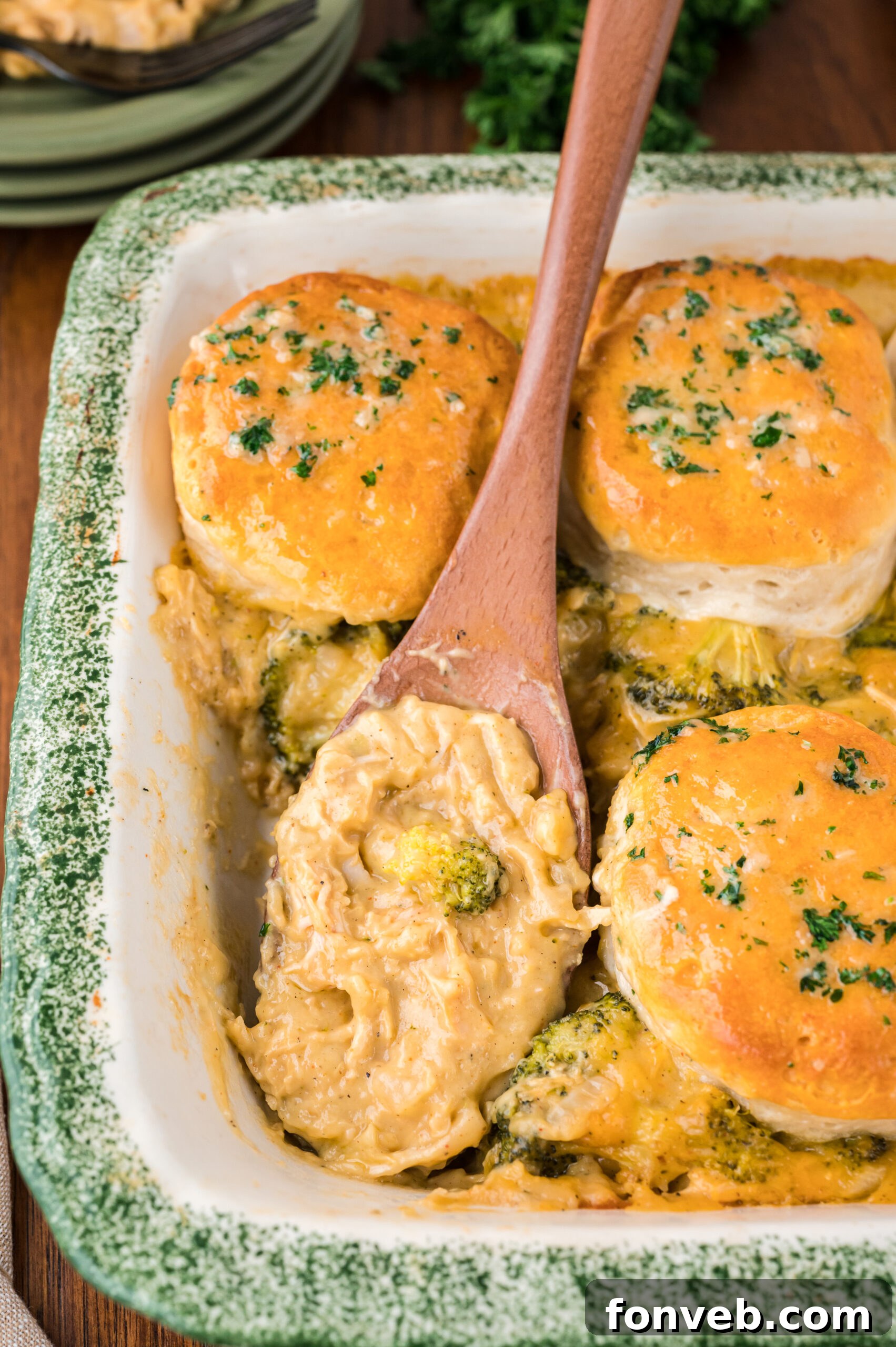 Close up view of a wooden spoon removing a serving of Broccoli Cheddar Biscuit Casserole.