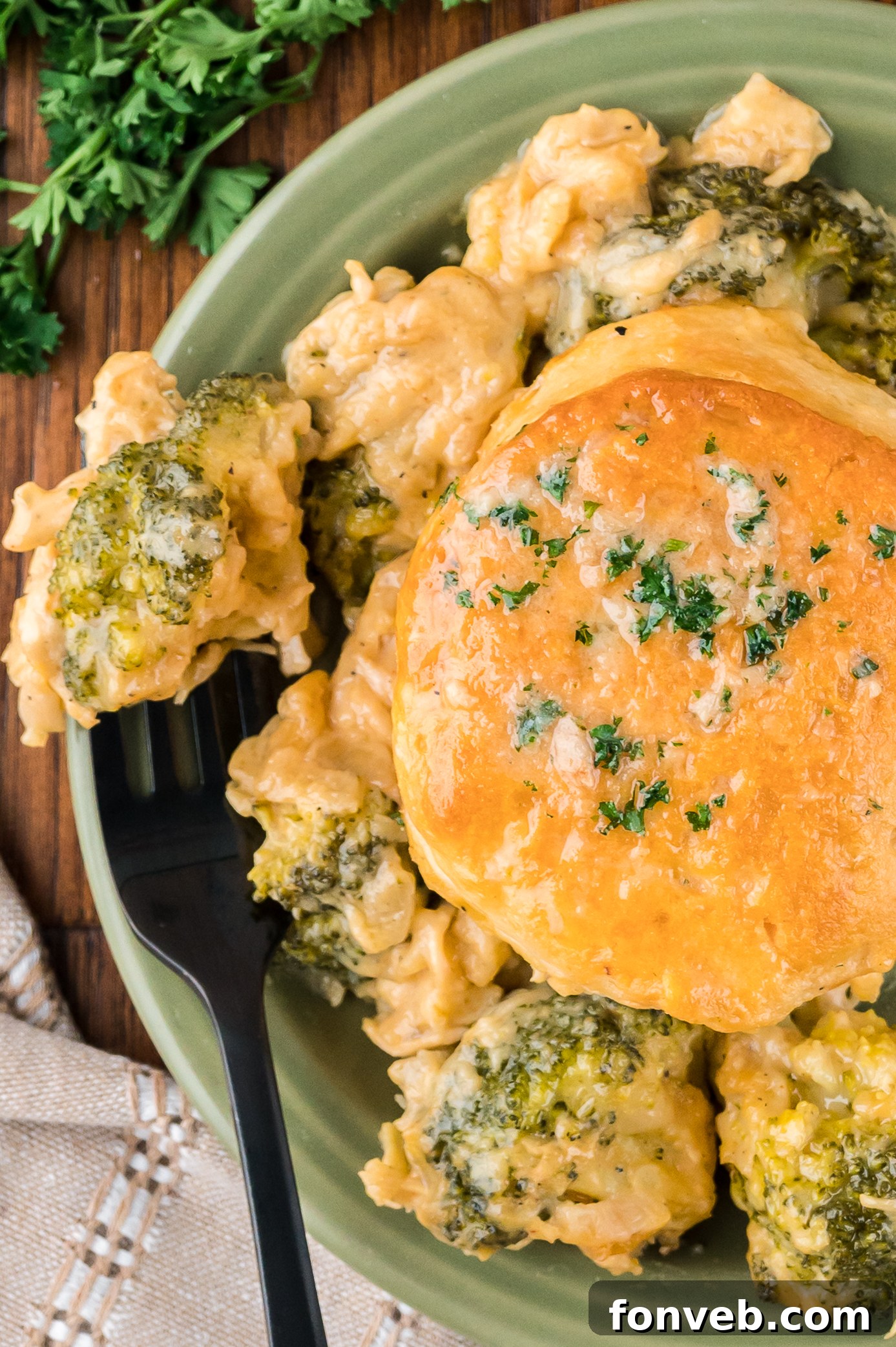 Overhead view of a serving of Broccoli Cheddar Biscuit Casserole on a green plate served with a black fork.