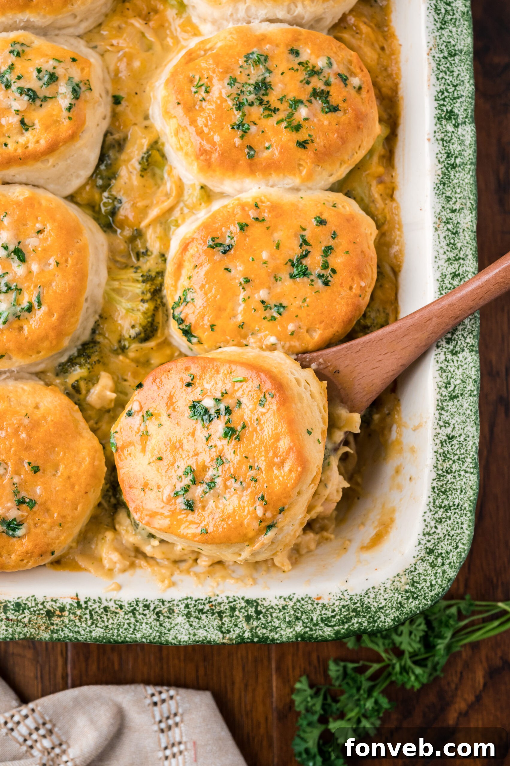 Overhead view of a wooden spoon removing a serving of Broccoli Cheddar Biscuit Casserole.