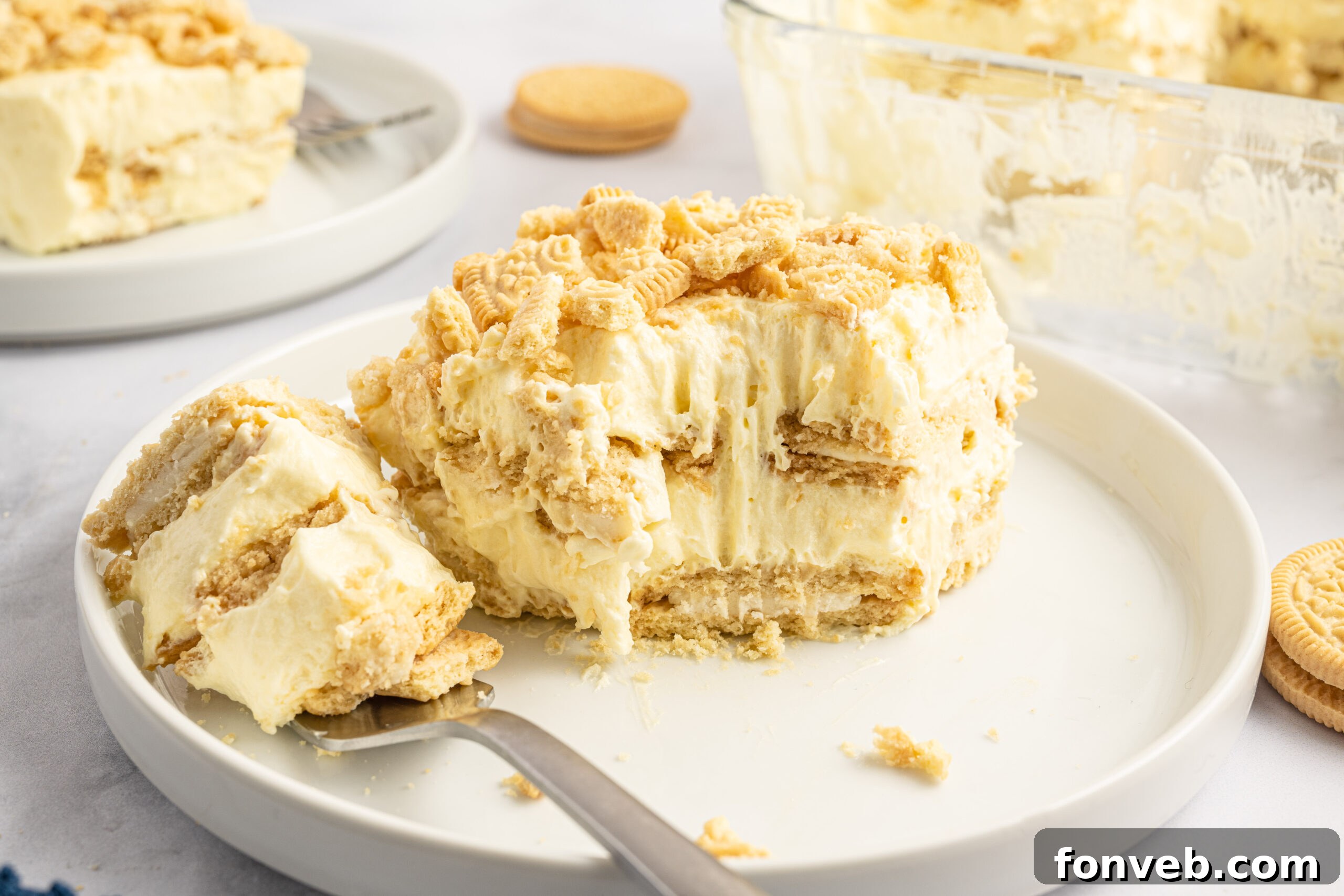 Golden Oreo No-Bake Delight 20 Front view of a slice of Golden Oreo Icebox Cake on a white plate with a bite removed by a silver fork.