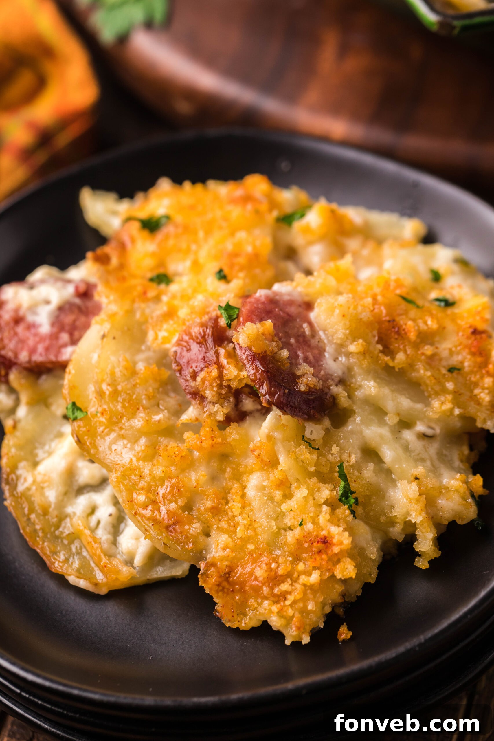 Creamy Sausage and Potato Gratin 20 Close up view of a serving of Au Gratin Potatoes & Ham on a black plate.