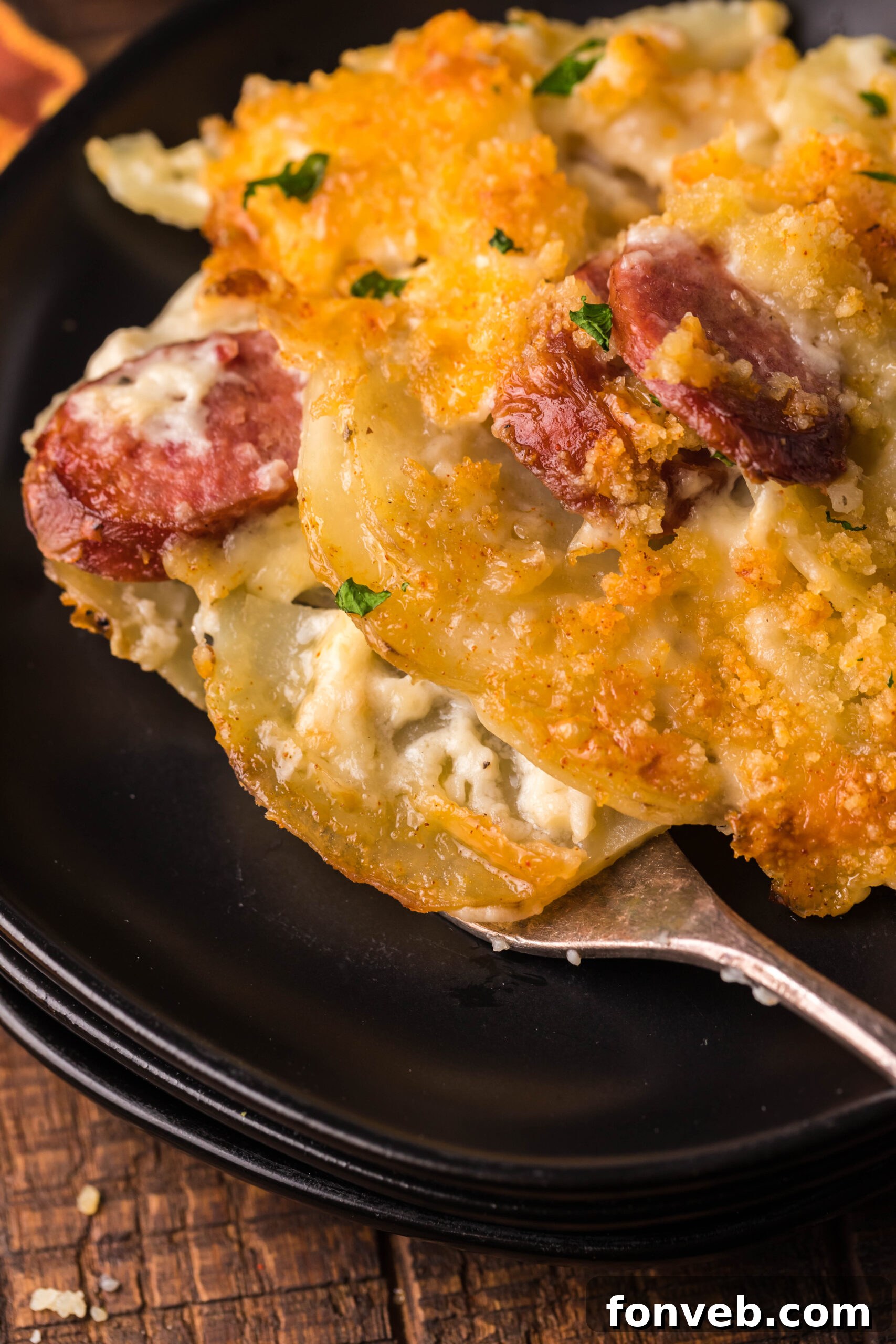 Creamy Sausage and Potato Gratin 22 Close up view of a serving of Au Gratin Potatoes & Ham on a black plate served with a silver fork.