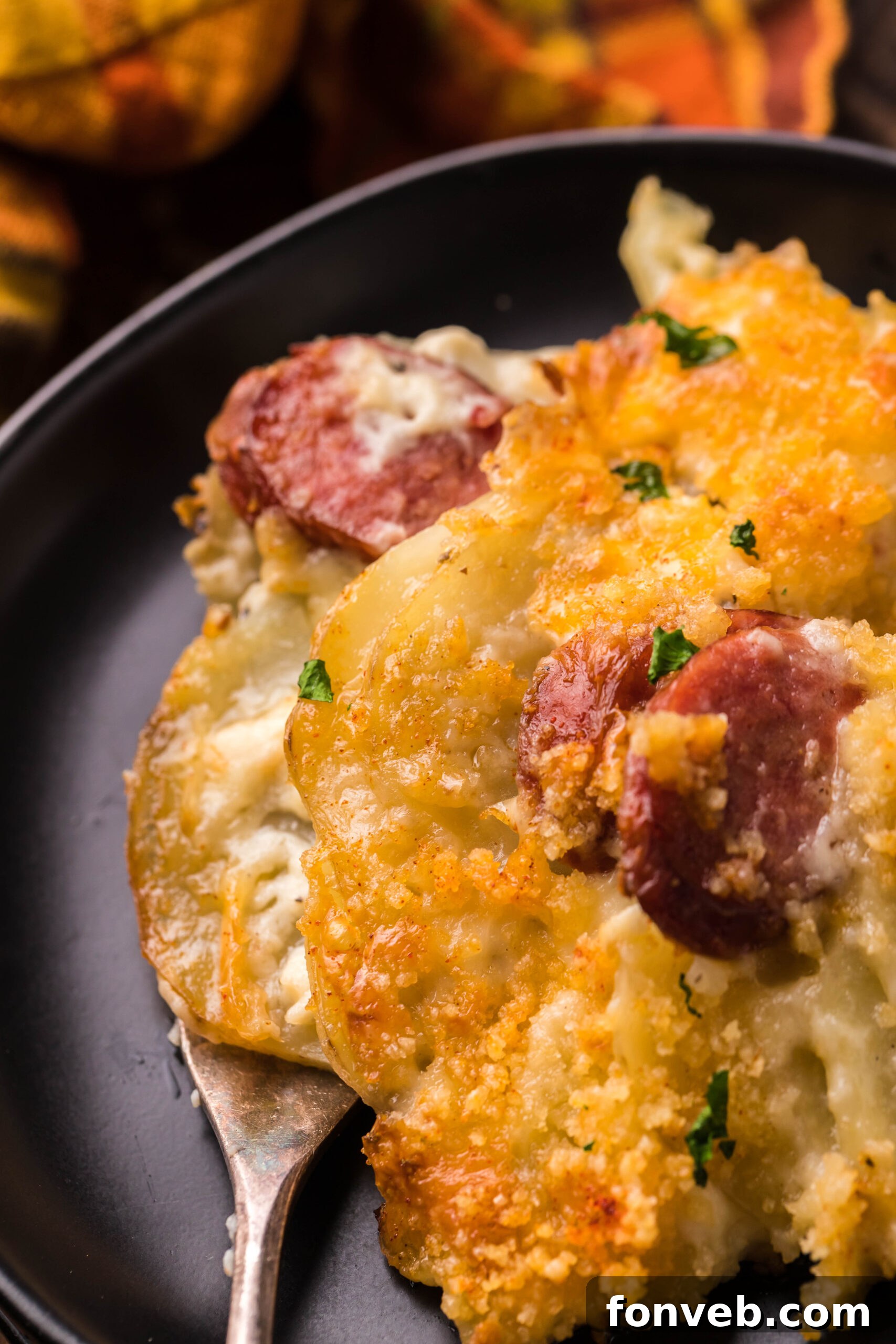 Creamy Sausage and Potato Gratin 23 Close up view of a serving of Au Gratin Potatoes & Ham on a black plate served with a silver fork.