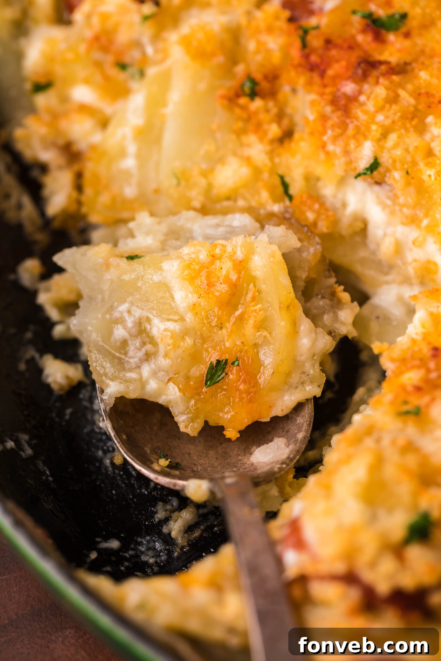 Creamy Sausage and Potato Gratin 9 Au Gratin Potatoes & Sausage in a cast iron skillet with a spoon scooping some
