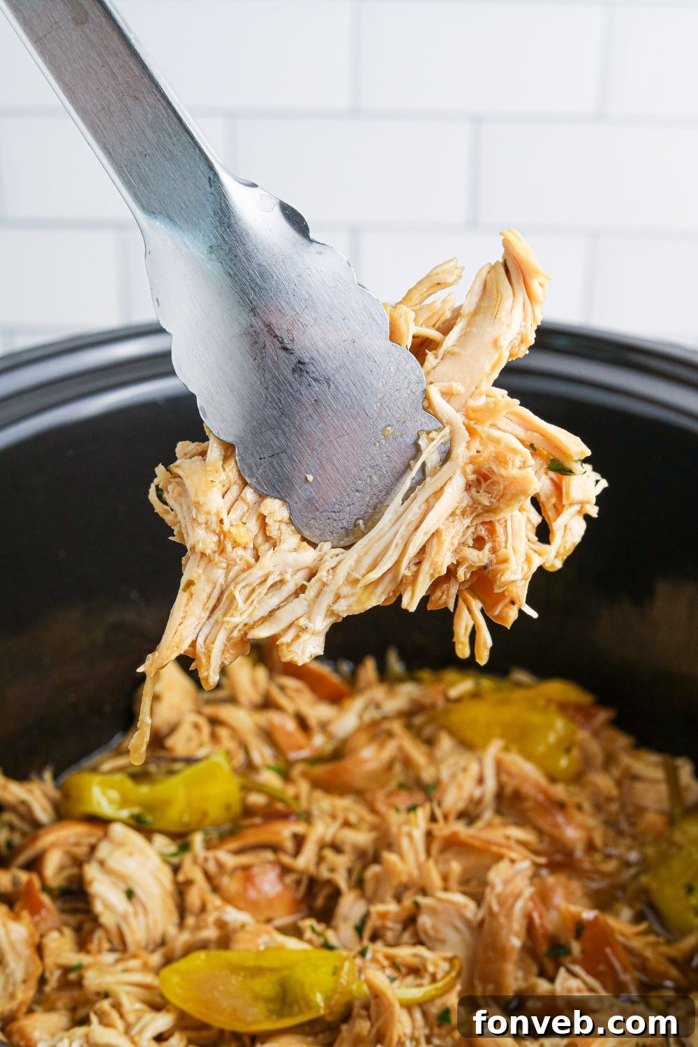 tongs with shredded chicken in it over the mississippi chicken in crockpot 