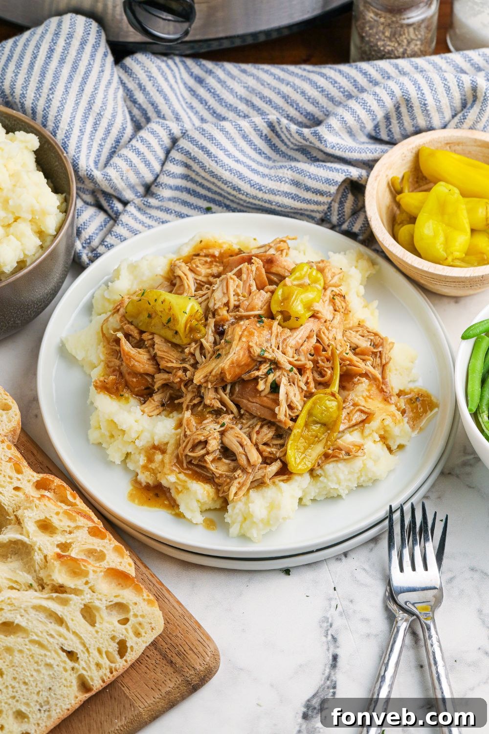 mashed potatoes and chicken on plate with peppers and bread around it on table 