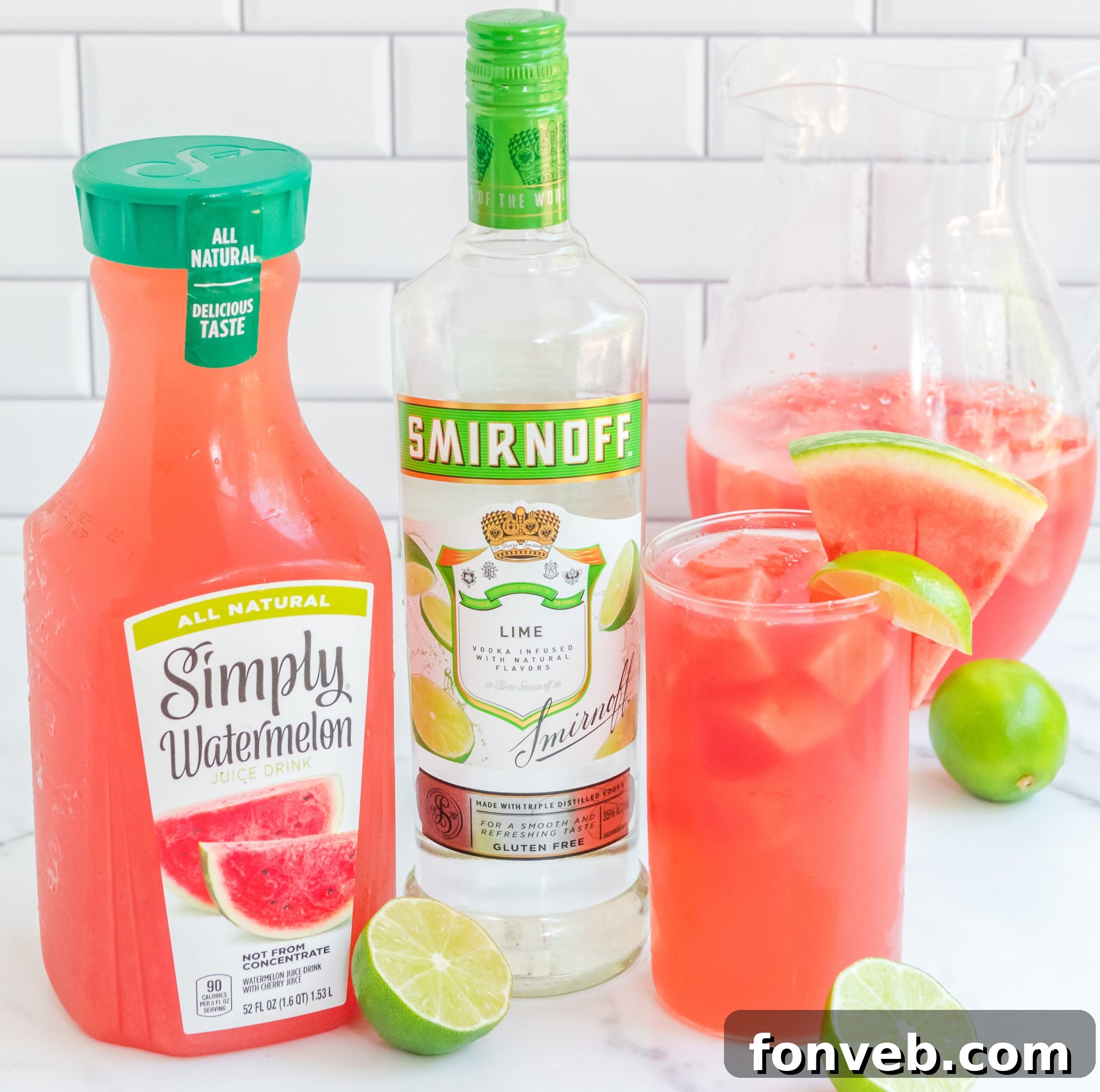 Front view of Watermelon Cocktail in a clear glasses garnished with lime and watermelon slices next wo watermelon juice bottle and a vodka bottle