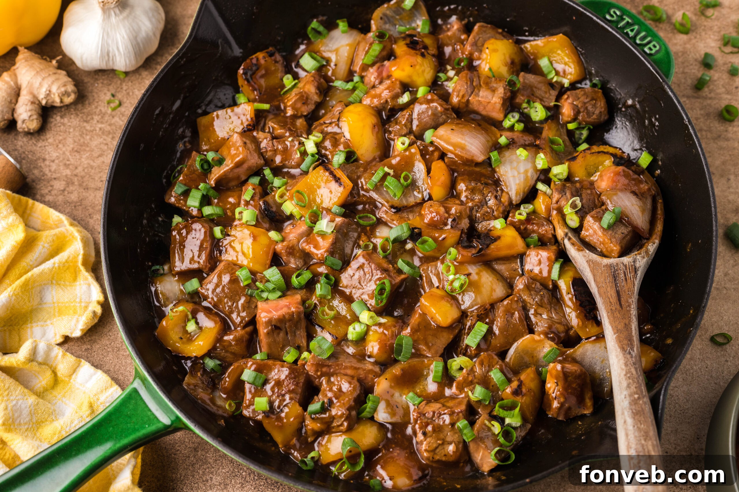 Front view of Teriyaki Steak Bites in a black and green skillet with a wooden spoon in the pan,