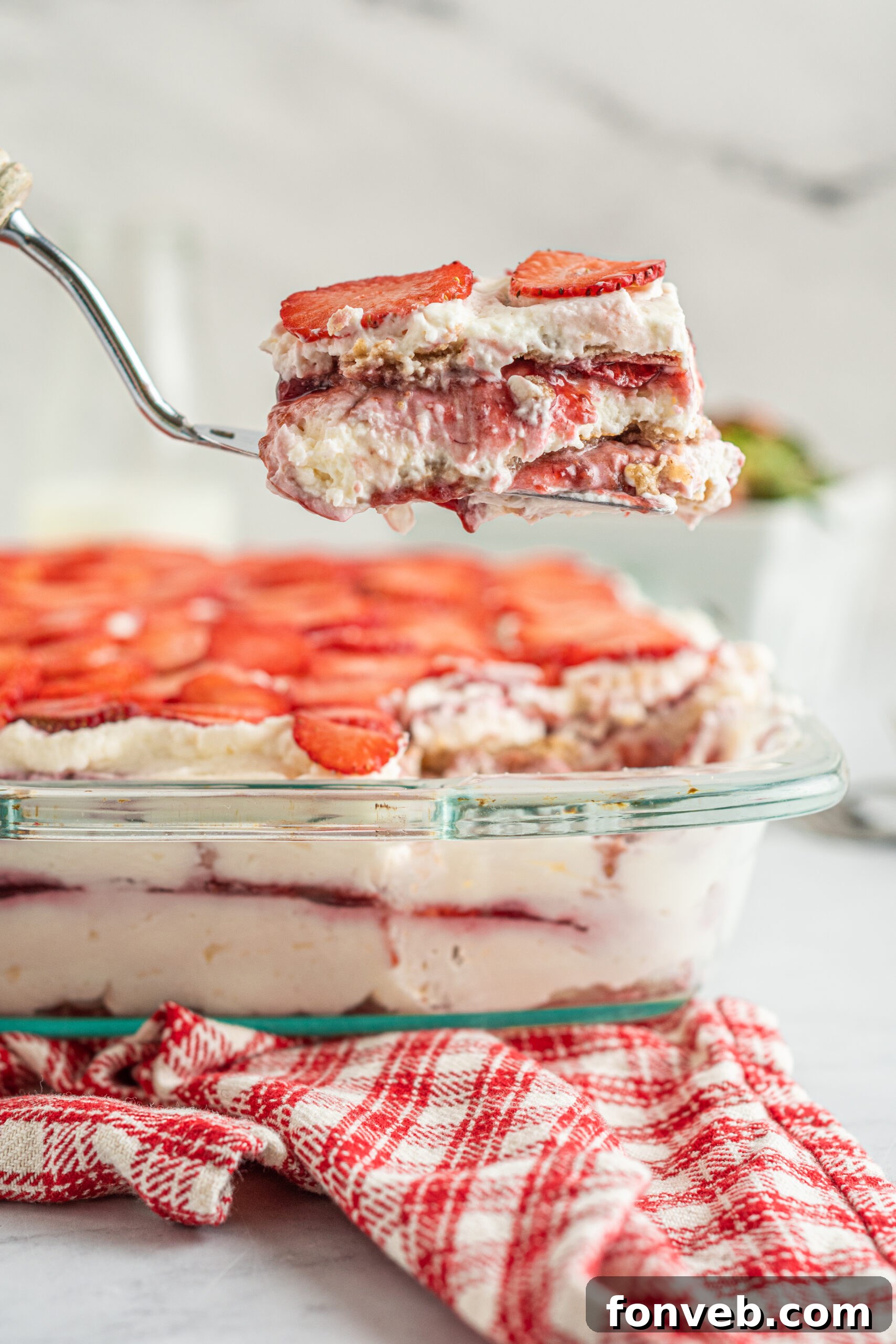 Strawberry Icebox Cake in a baking dish with a piece being removed with a silver spatula.