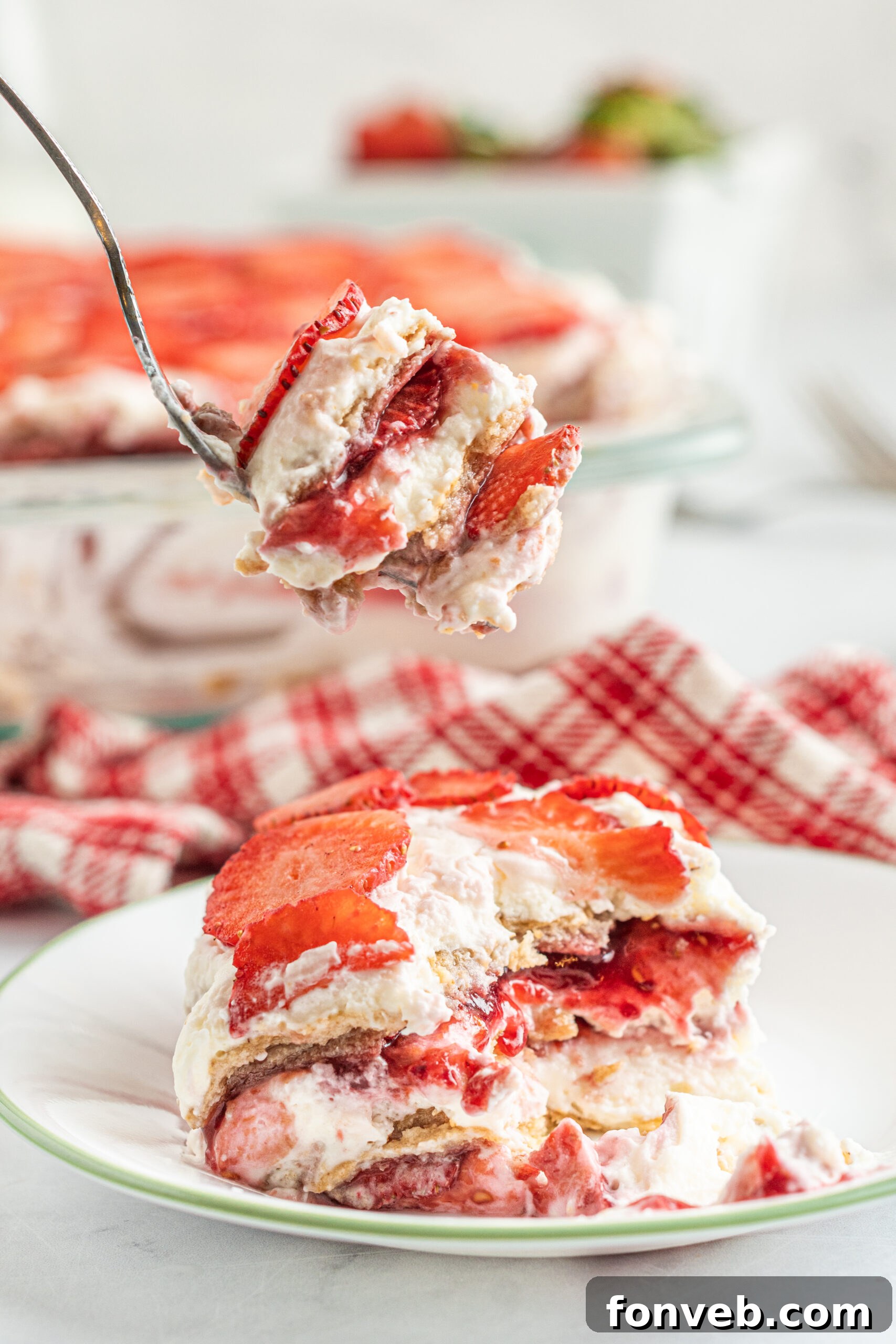 A piece of Strawberry Icebox Cake on a white and green plate with a bite being removed with a silver fork. 