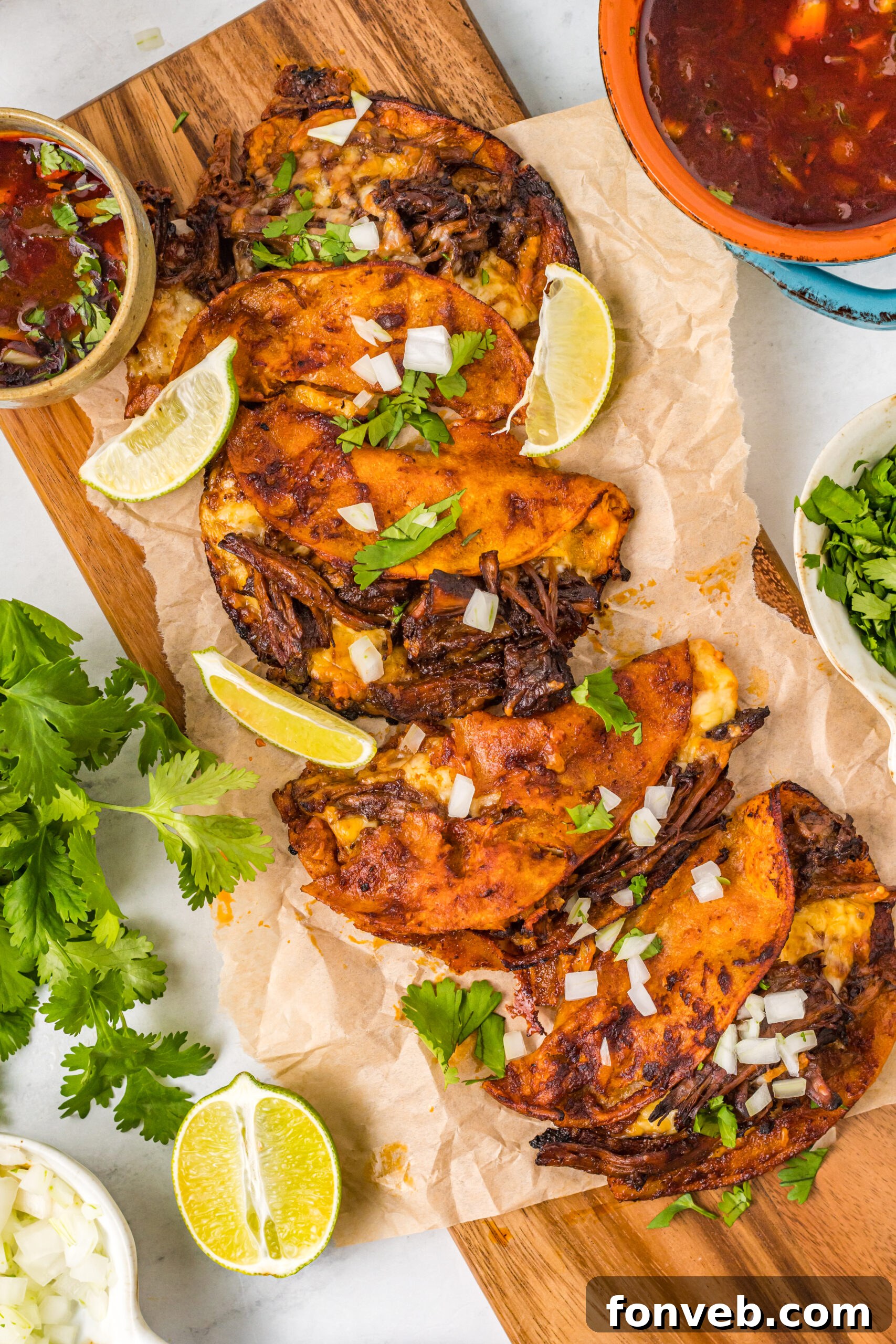 Overhead view of Birria Tacos on a wooden board garnished with onion and cilantro.