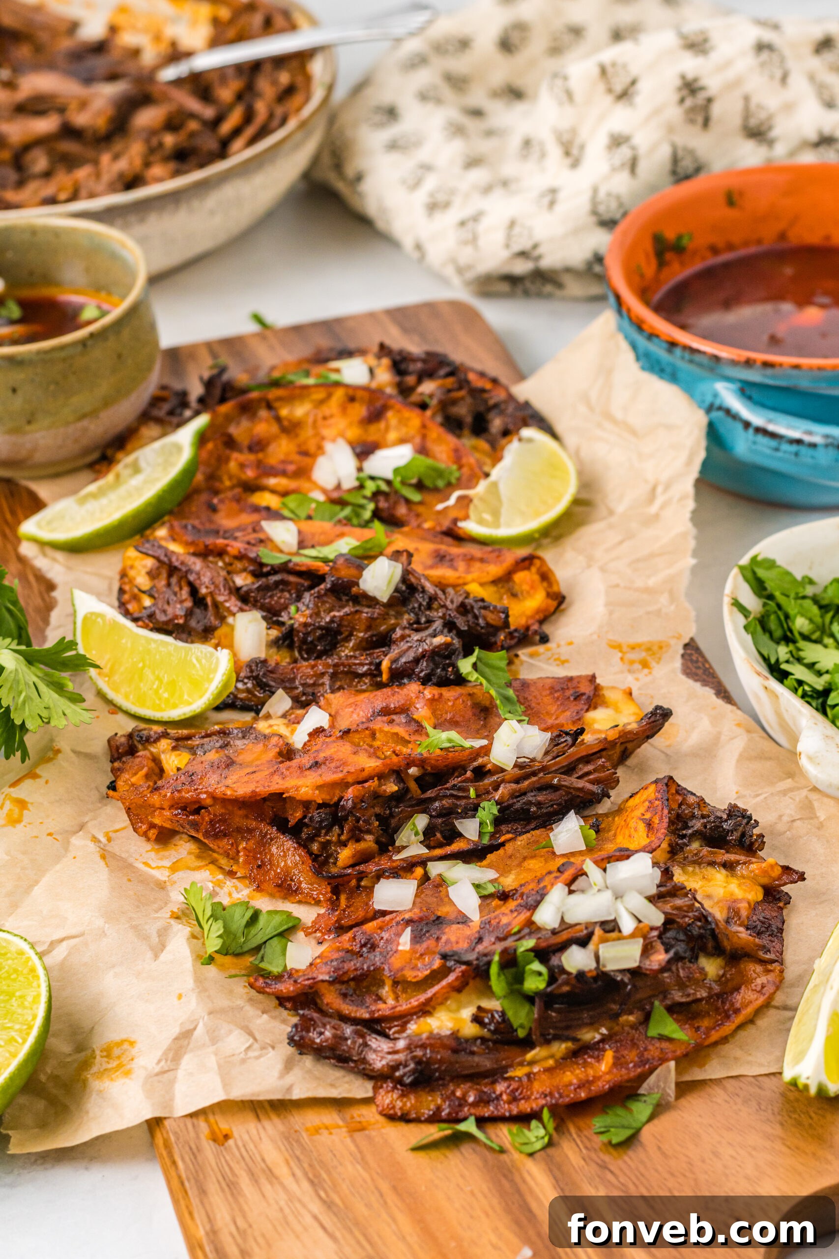 Front view of Birria Tacos on a wooden board garnished with onion and cilantro.