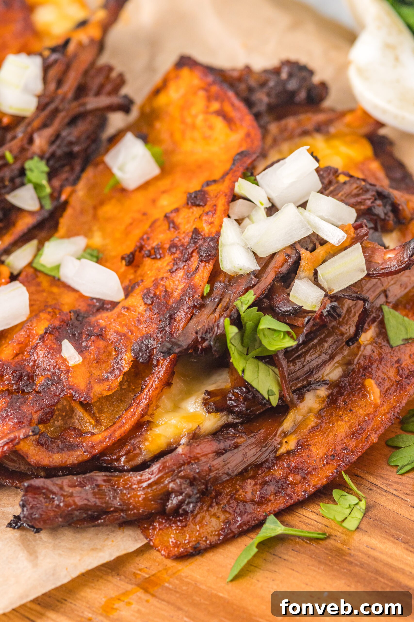 Overhead view of Birria Tacos on a wooden board garnished with onion and cilantro.