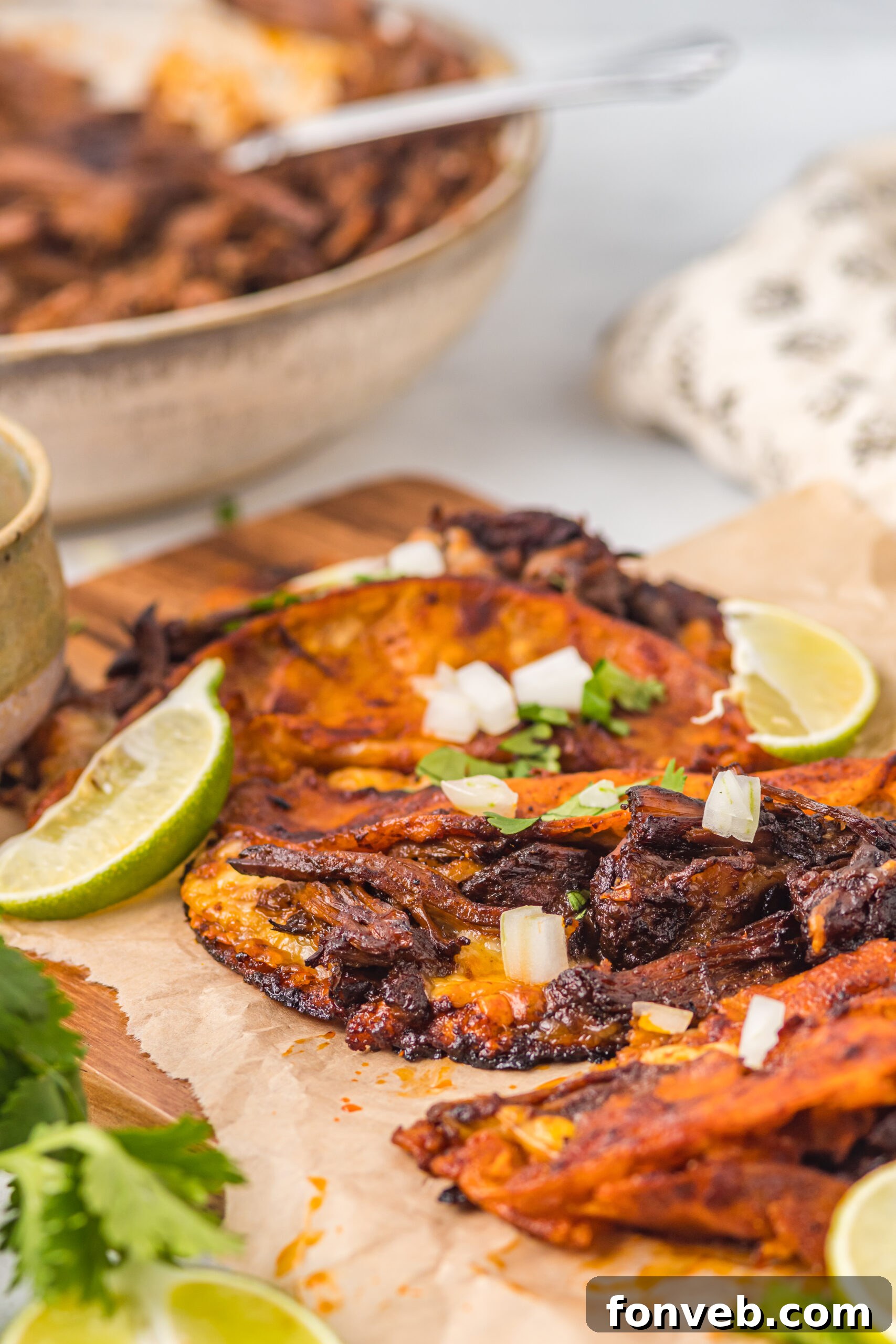 Front view of Birria Tacos on a wooden board garnished with onion and cilantro.