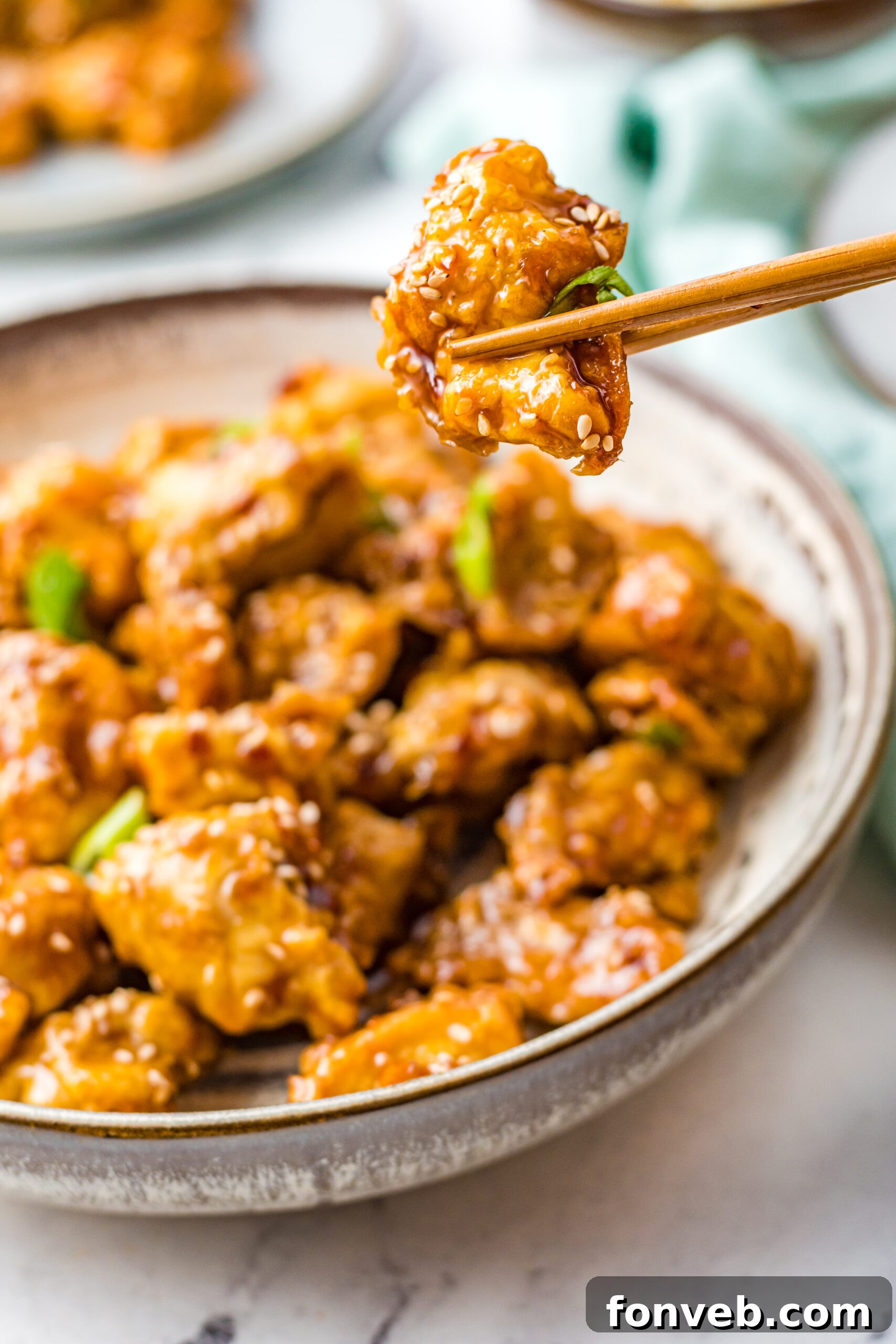 Close up view of chopsticks hold a piece of Air Fryer General Tsos Chicken.
