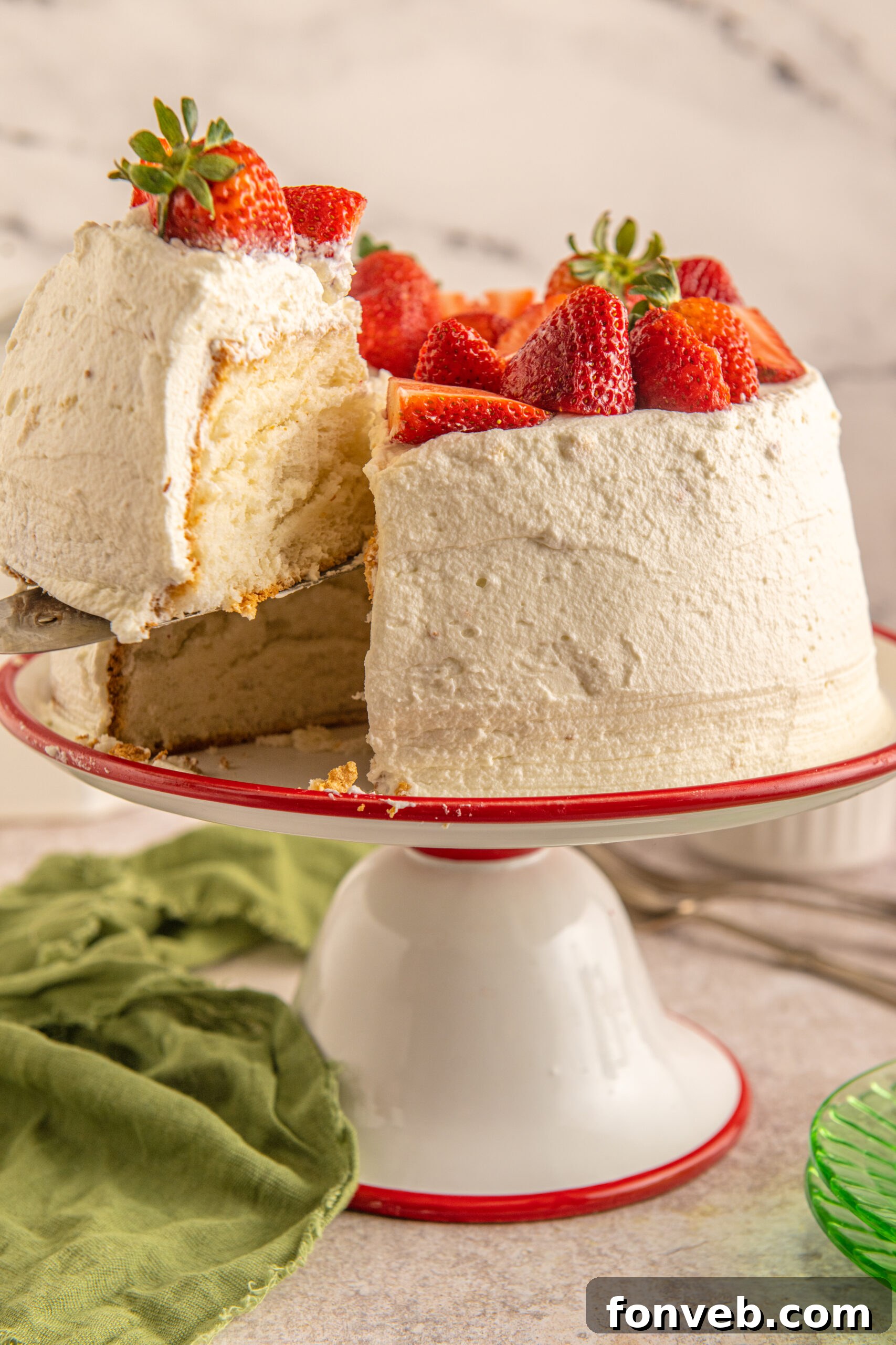 A piece of Strawberry Angel Food Cake being removed from a red and white cake stand with a silver spatula. 