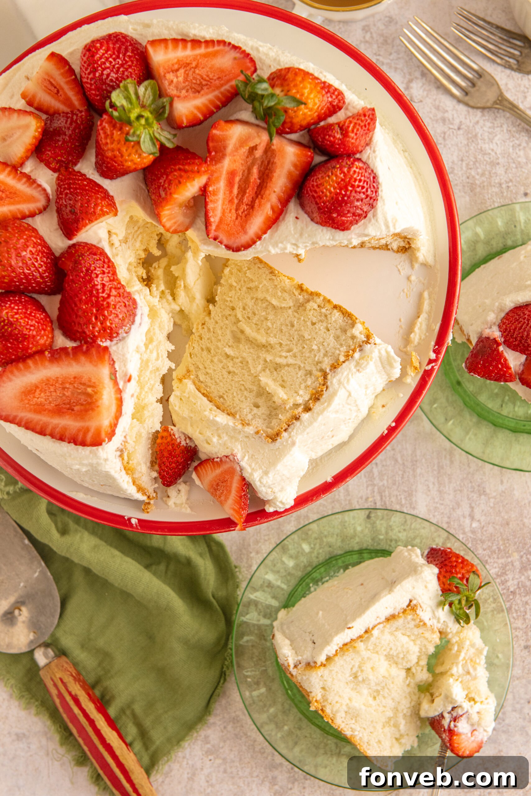 Overhead view of a cut piece of Strawberry Angel Food Cake on a white and red cake stand with two pieces served on green plates in the background. 