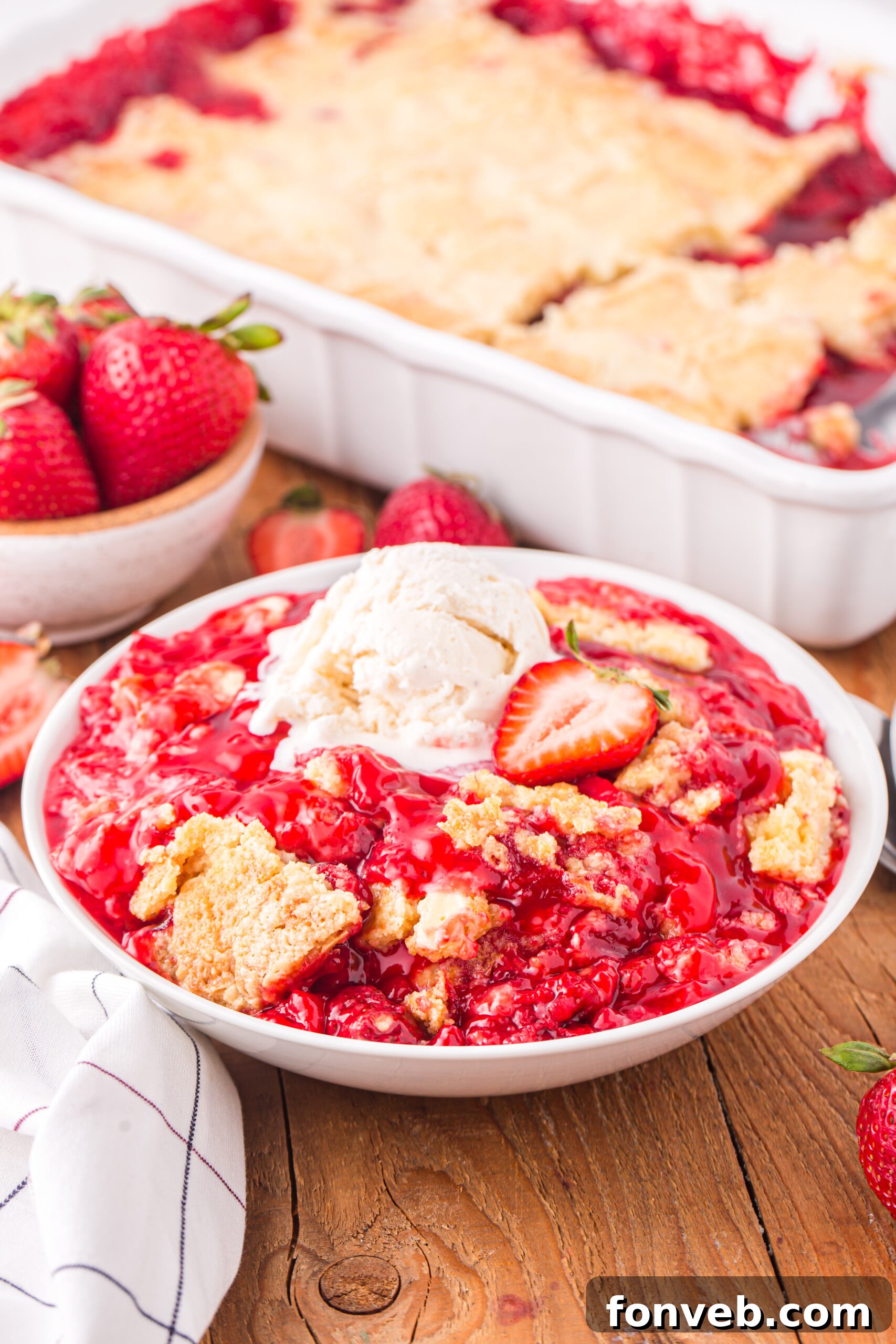 Front view of a serving of Strawberry Dump Cake in a white bowl topped with a scoop of ice cream.
