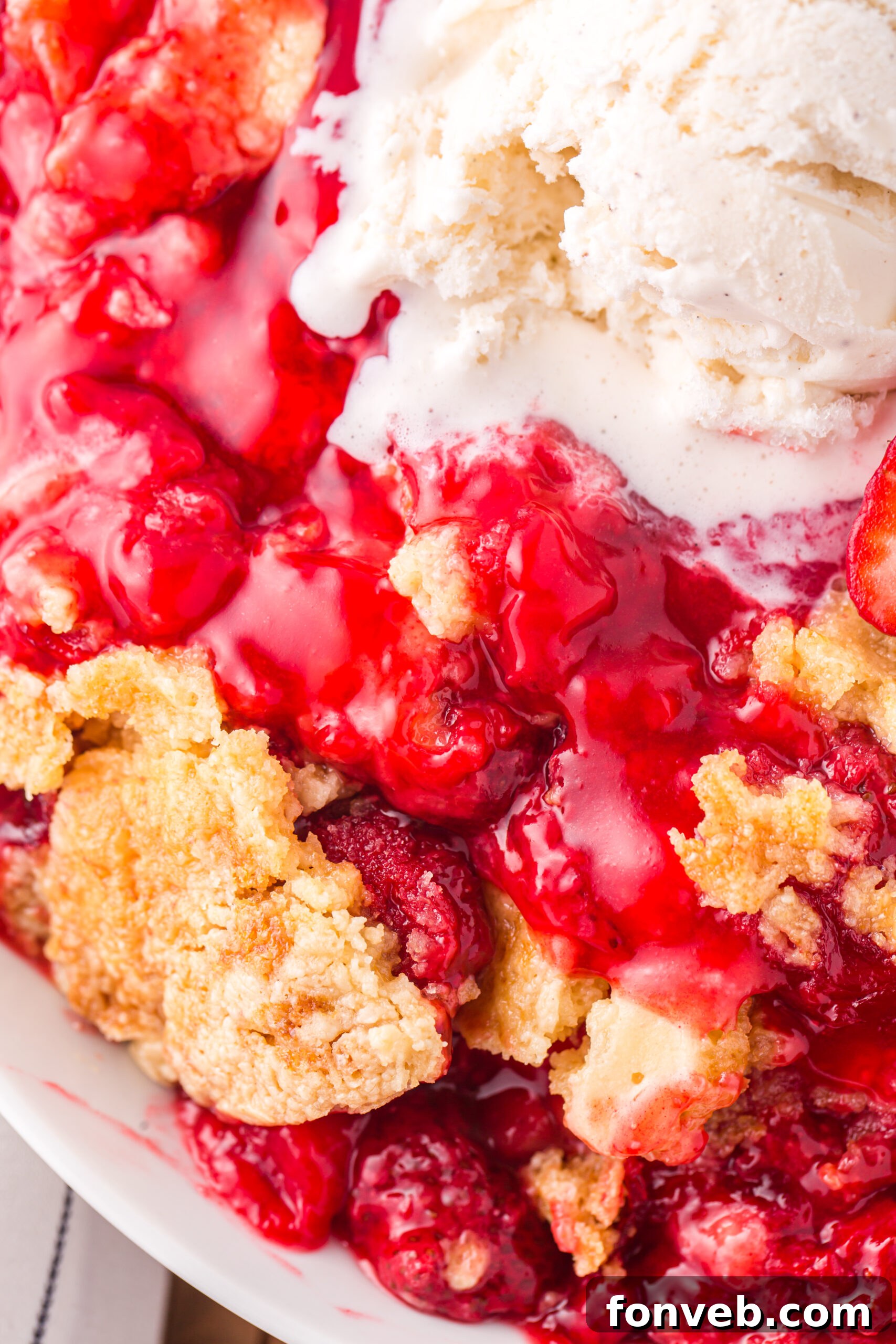 Close up view of a serving of Strawberry Dump Cake in a white bowl topped with a scoop of ice cream.