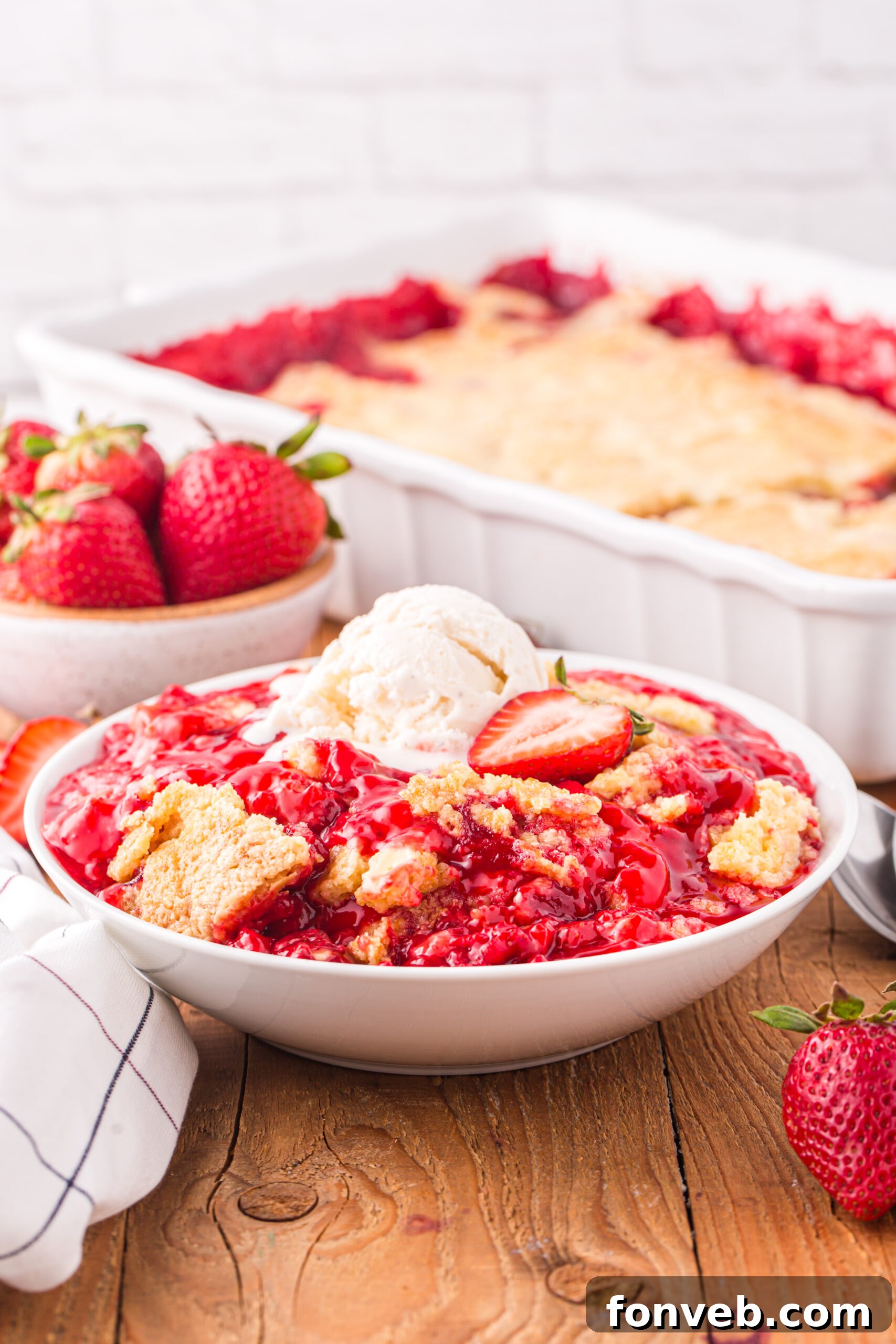 Front view of a serving of Strawberry Dump Cake in a white bowl topped with a scoop of ice cream.