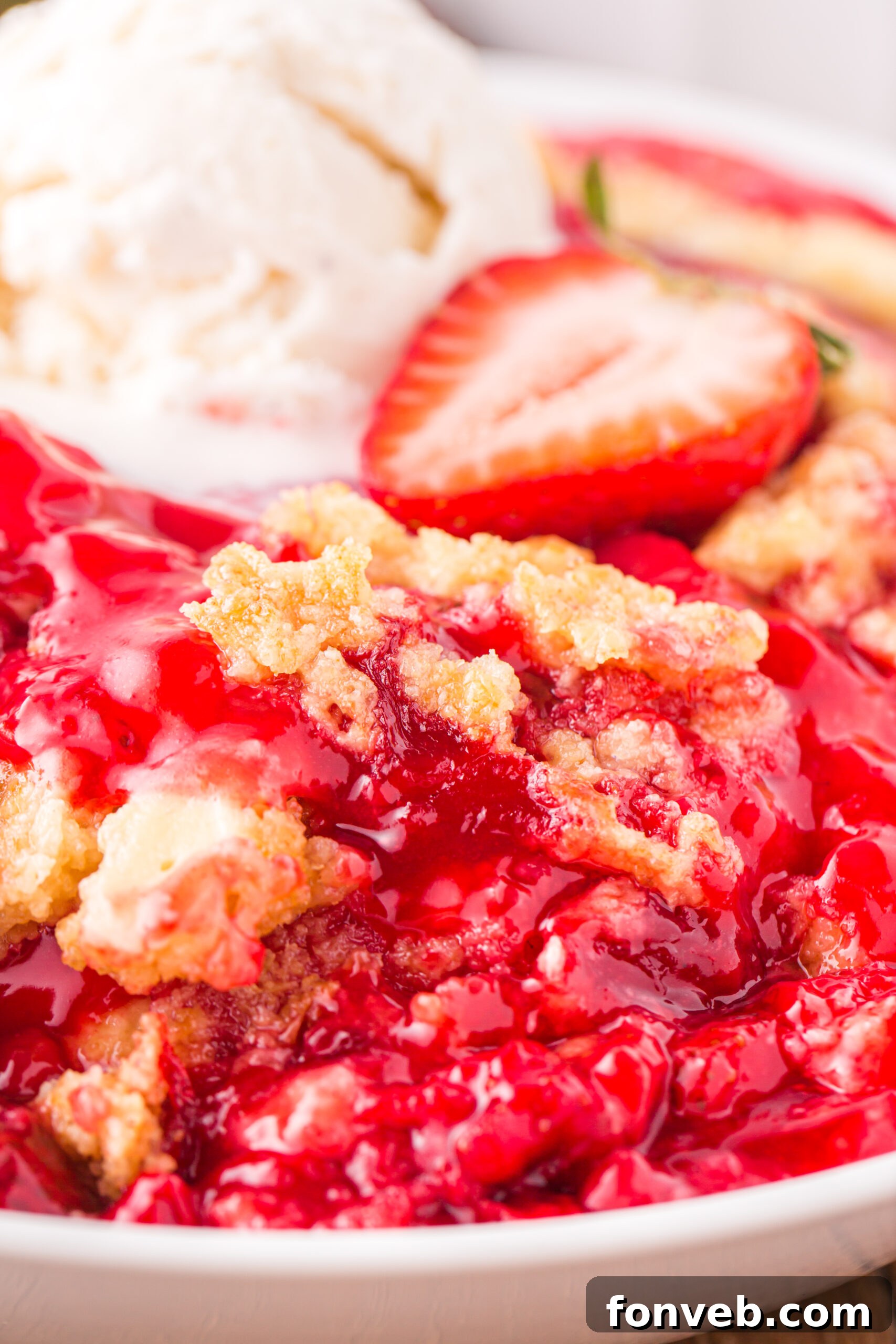 Close up view of a serving of Strawberry Dump Cake in a white bowl topped with a scoop of ice cream.