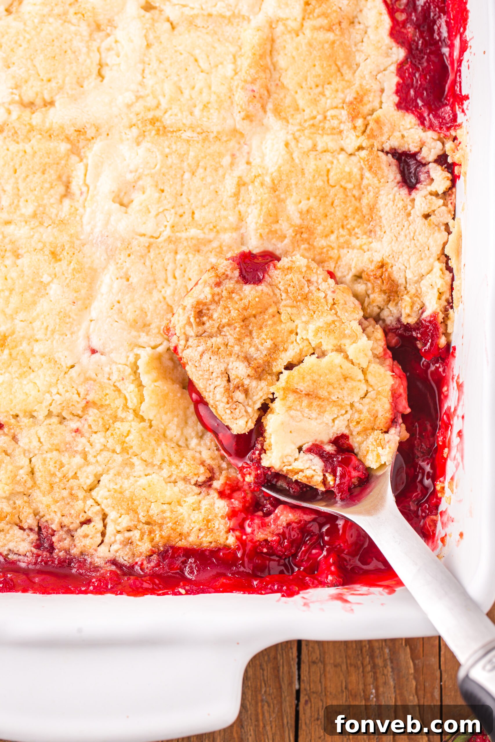 Close up view of a serving spoon removing a serving of Strawberry Dump Cake.