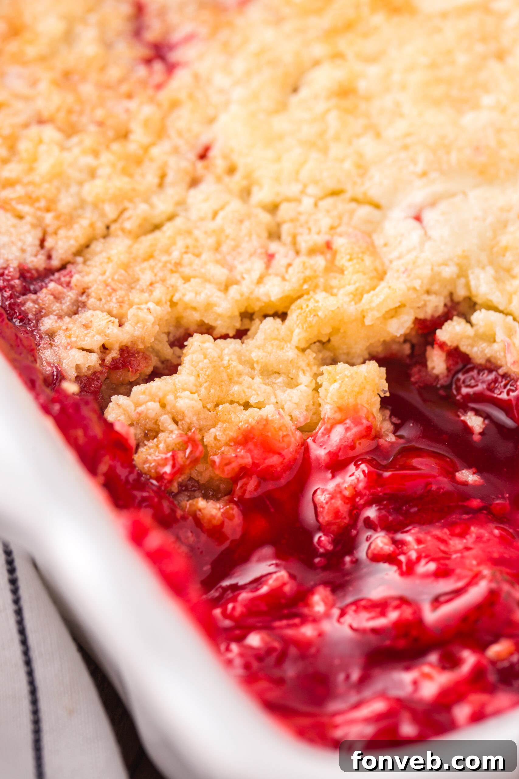 Close up view of Strawberry Dump Cake in a white baking dish with a serving removed.