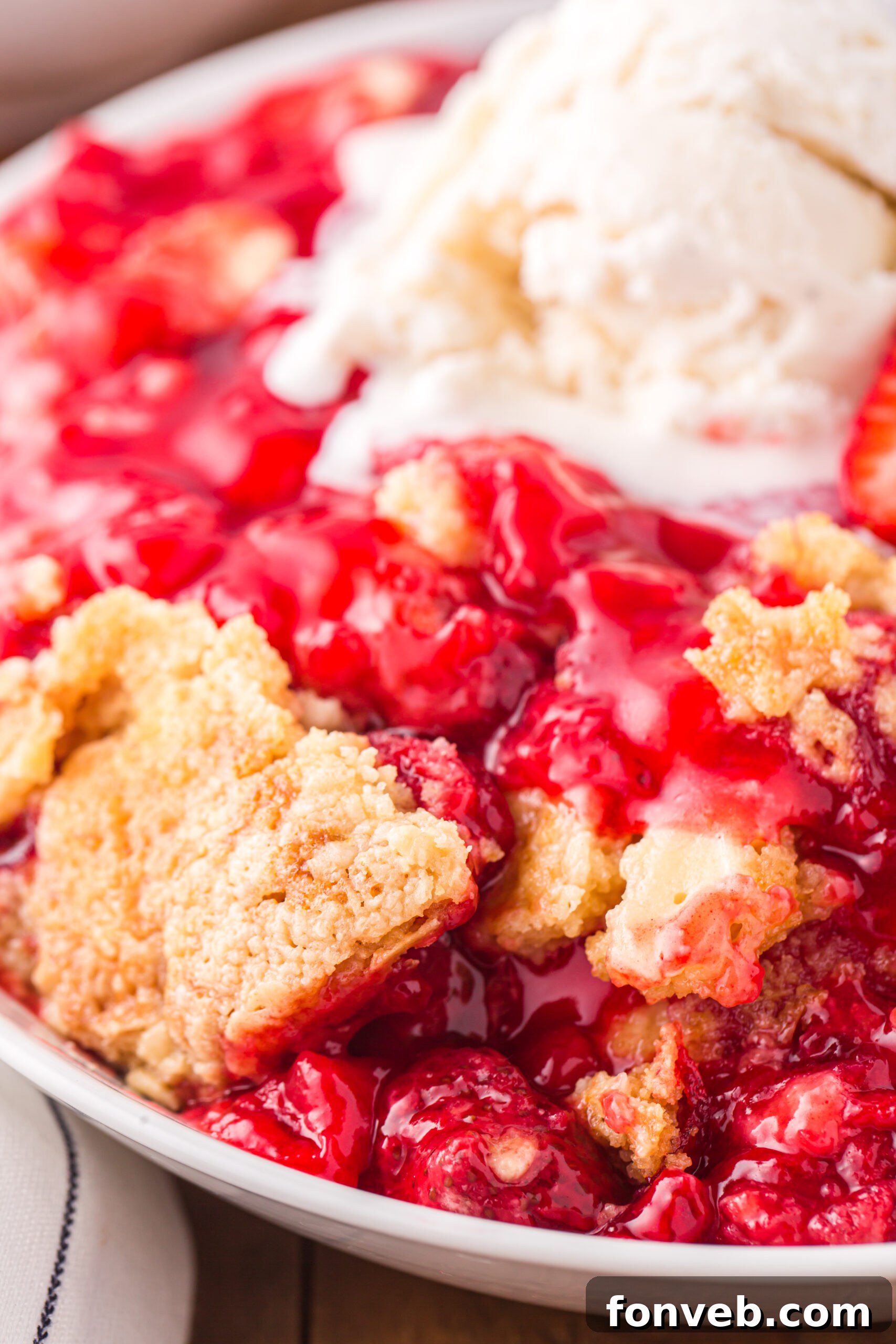Close up view of a serving of Strawberry Dump Cake in a white bowl topped with a scoop of ice cream.