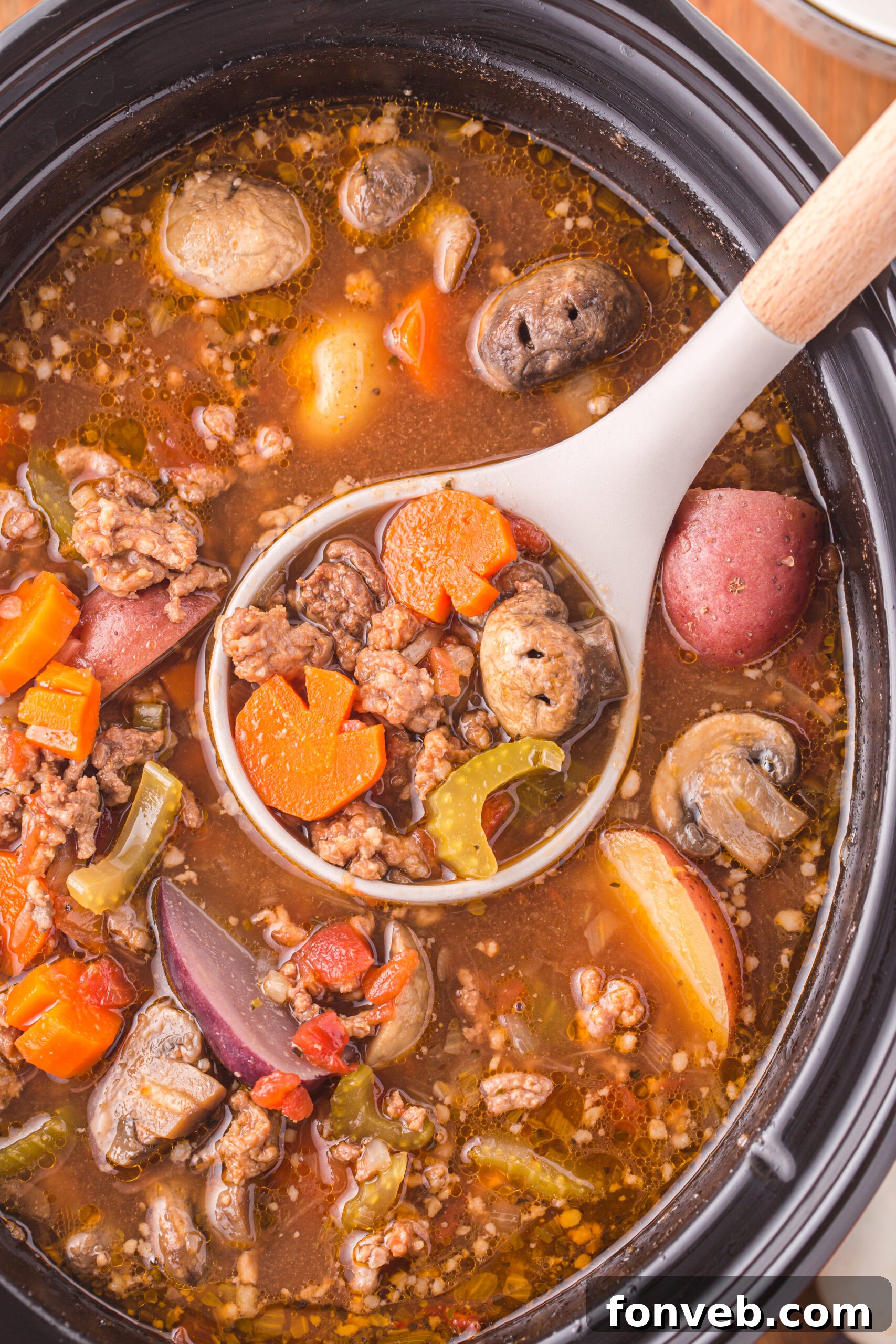Overhead view of a serving spoon removing a portion of Witches Brew Stew, highlighting the chunky ingredients.