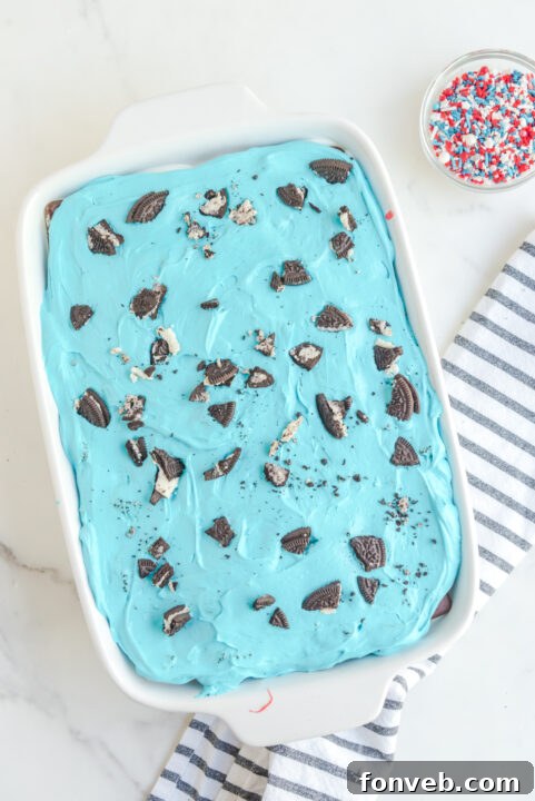 Topping the cake with blue filling, crushed Oreos, and patriotic sprinkles.