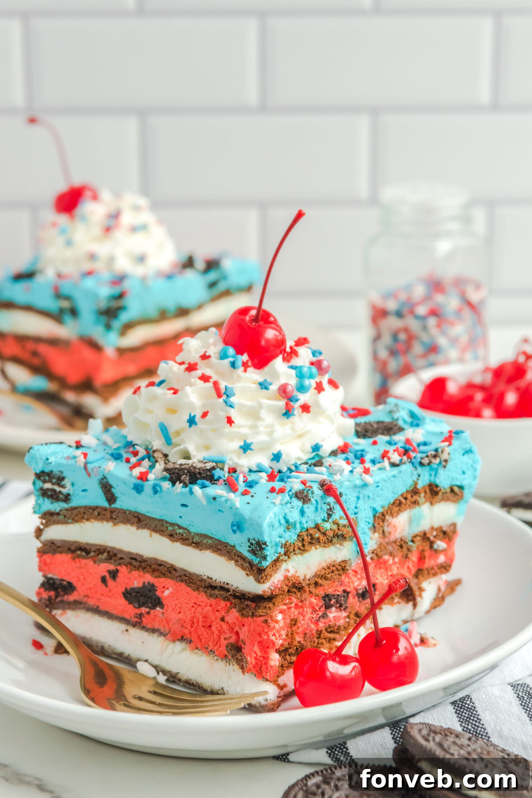 Front view of a slice of Patriotic Ice Cream Sandwich Cake topped with whipped cream and cherry on a white plate.
